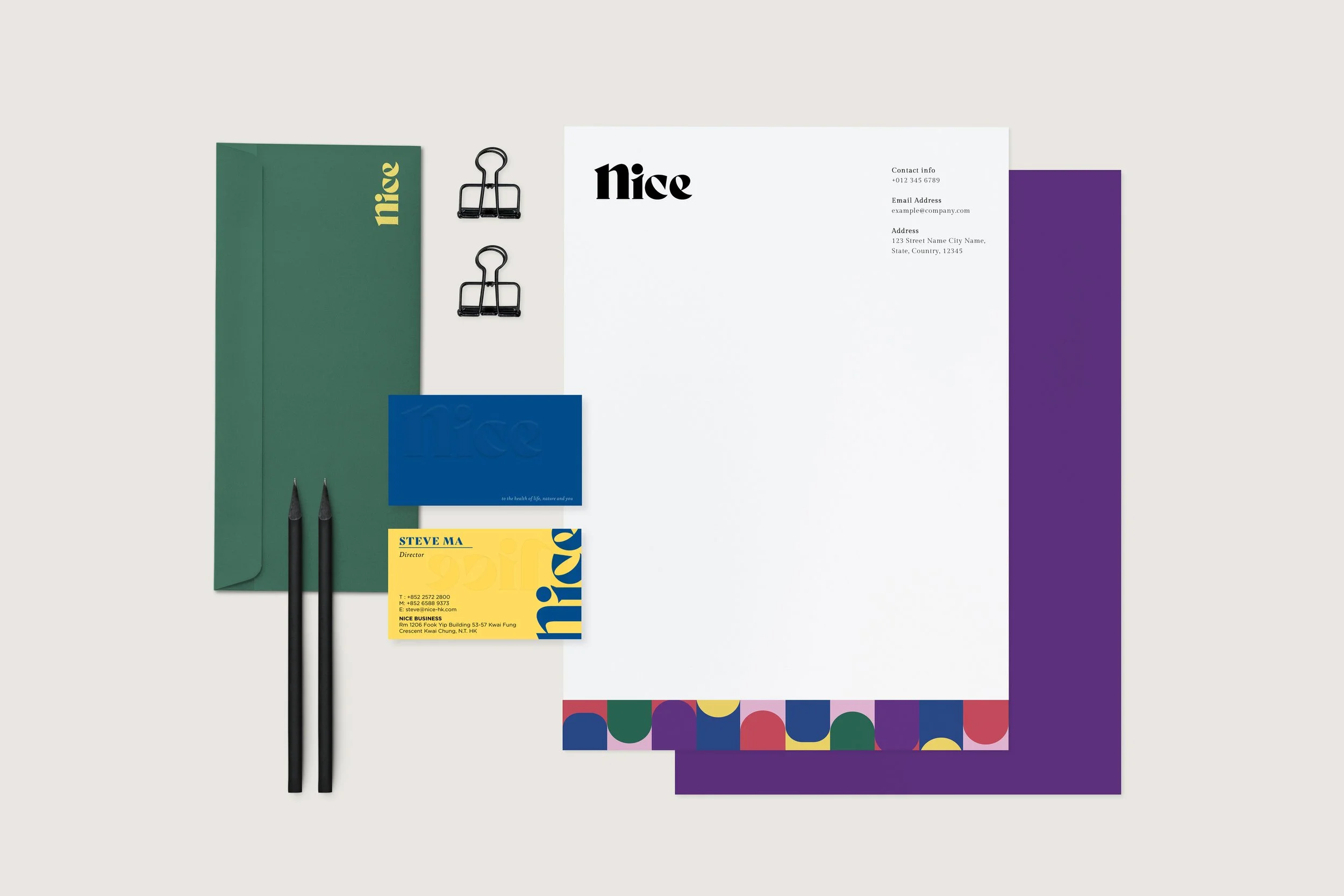 Flat lay of colorful office stationery, including a green folder, two black pens, a blue card, a yellow business card, two black binder clips, and various sheets of paper with colorful borders, arranged on a white background.