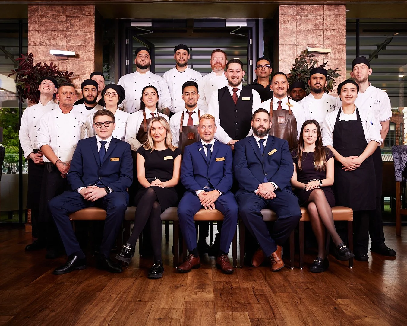 Group photo of restaurant staff, including chefs, waiters, and managers, posing indoors in a well-lit restaurant setting.