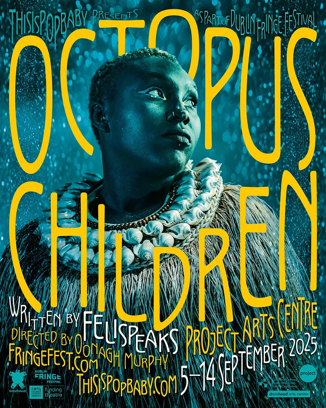 A promotional poster for 'This is pop baby,' Dublin Fringe Festival. It features a person with short hair, wearing tribal jewellery and a textured outfit, against a blue background with water droplets, shot in photo studio with beautiful lighting.