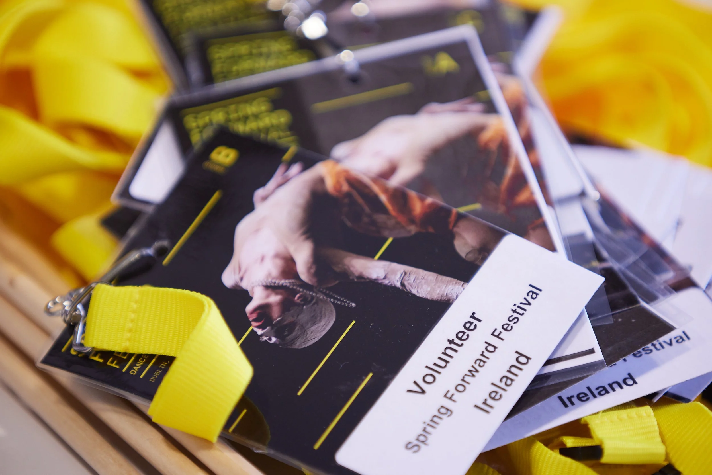 A stack of volunteer badges for Ireland's Spring Forwardward Festival, featuring a man on stage, with yellow lanyards attached.