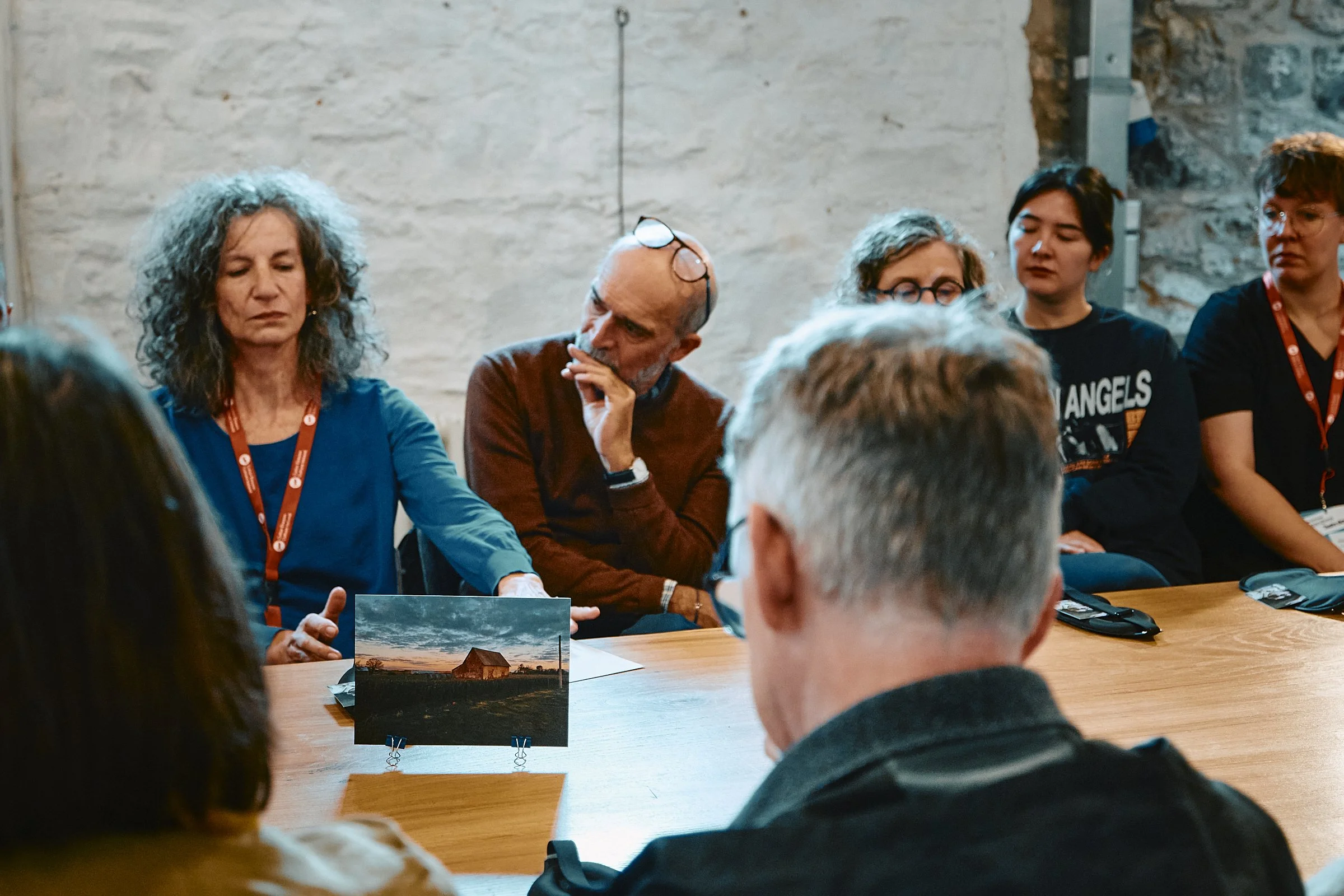 Group of people sitting around a table in a meeting or discussion, with a photo of a barn and sunset scenery on the table.