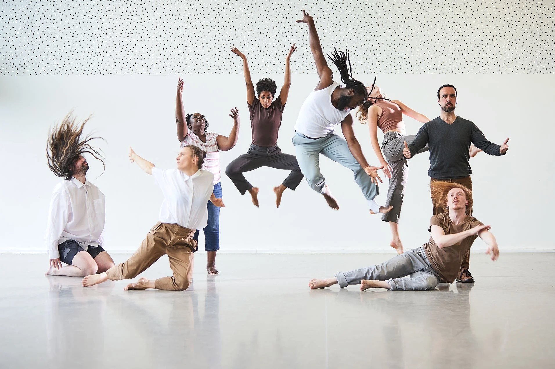 strong promotional image photo of a group of eight diverse people in various dance or movement poses indoors with a white speckled ceiling shooting in location with professional photography lighting.