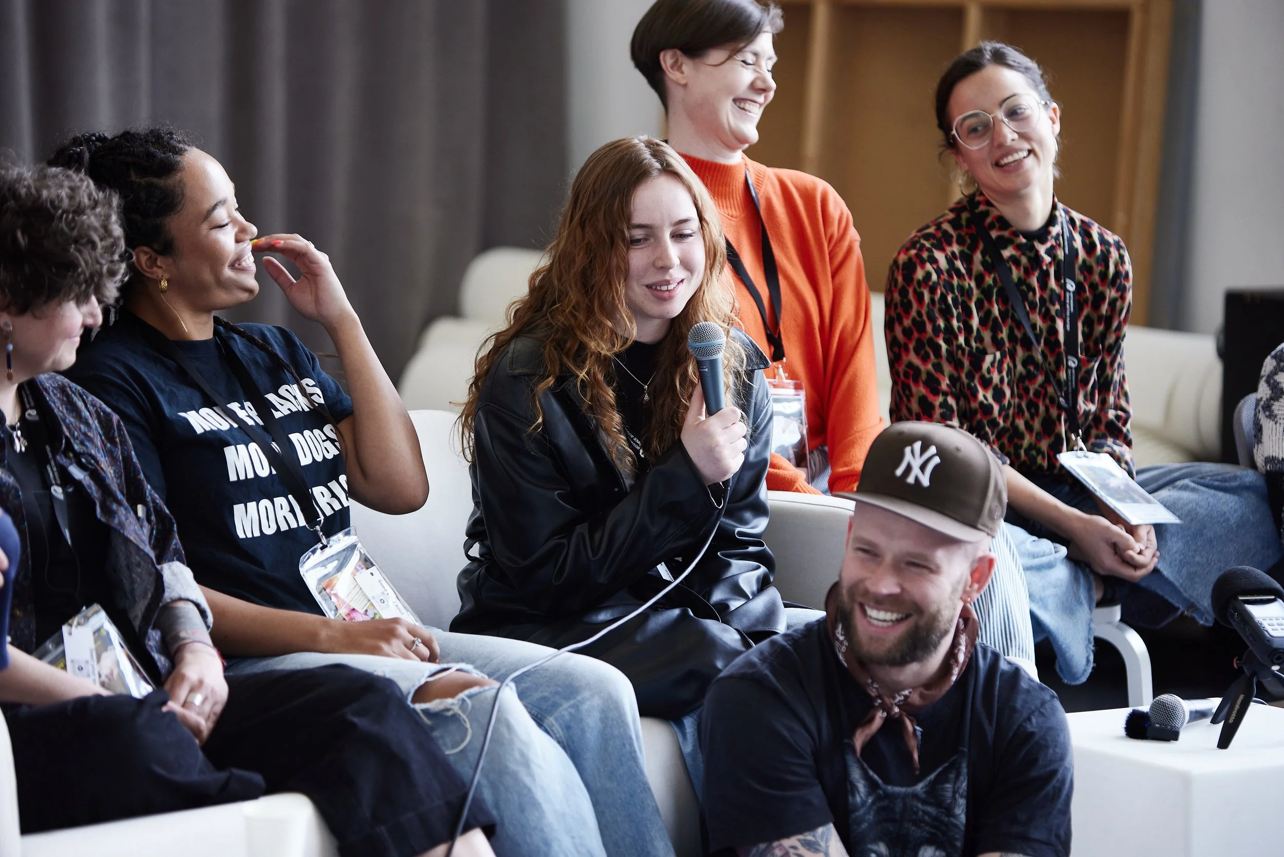 Group of diverse people sitting and laughing during a panel or discussion with one person holding a microphone.