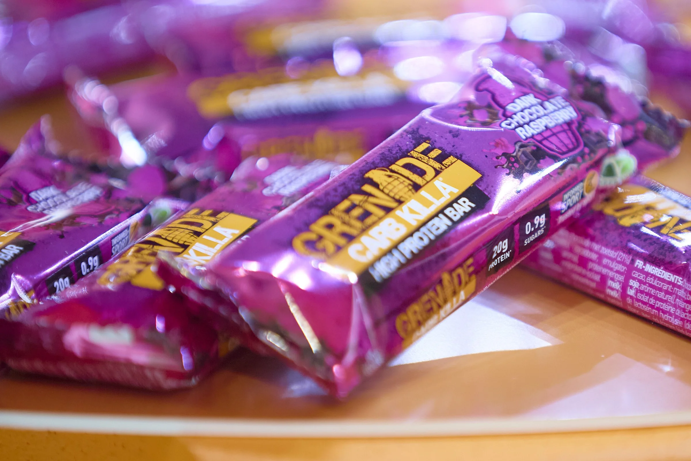 Multiple packs of Creende protein bars with purple packaging featuring a pink and purple design, placed on a wooden surface.