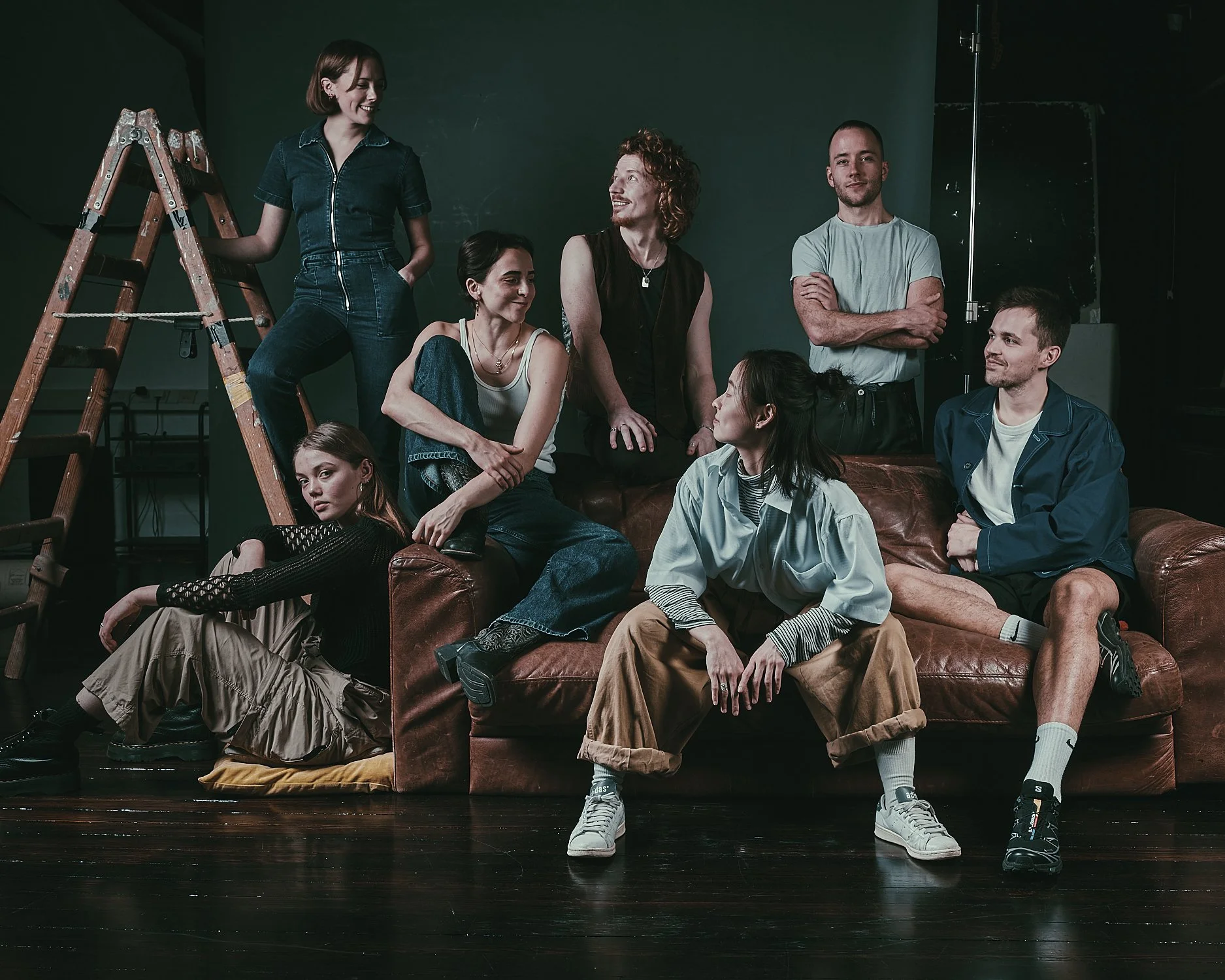 Advertising profession photo taken in  location of a group of professional dancers in casual clothing posing on and around a brown leather couch in a studio with a green wall background.
