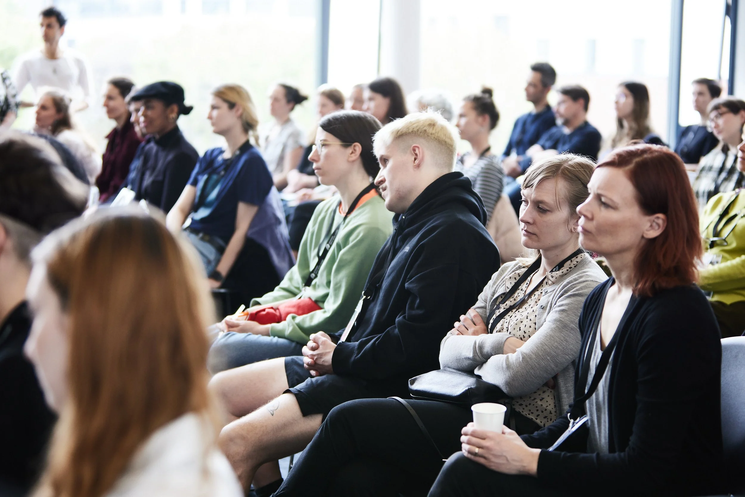 Audience attending a lecture or presentation in a conference room with large windows.