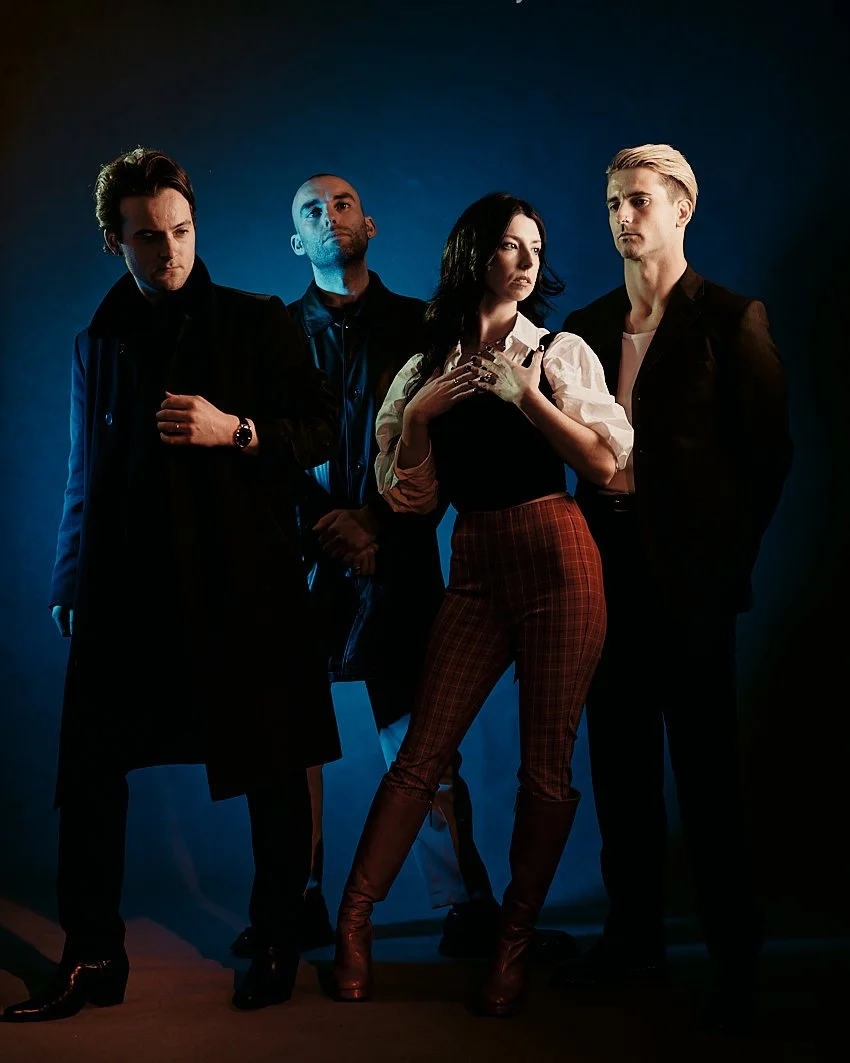Advertising high quality image of  music band "Soda Blond",  group of four people standing against a blue background, dressed in stylish and dark clothing, in a photo studio with high quality complex professional lighting setup.