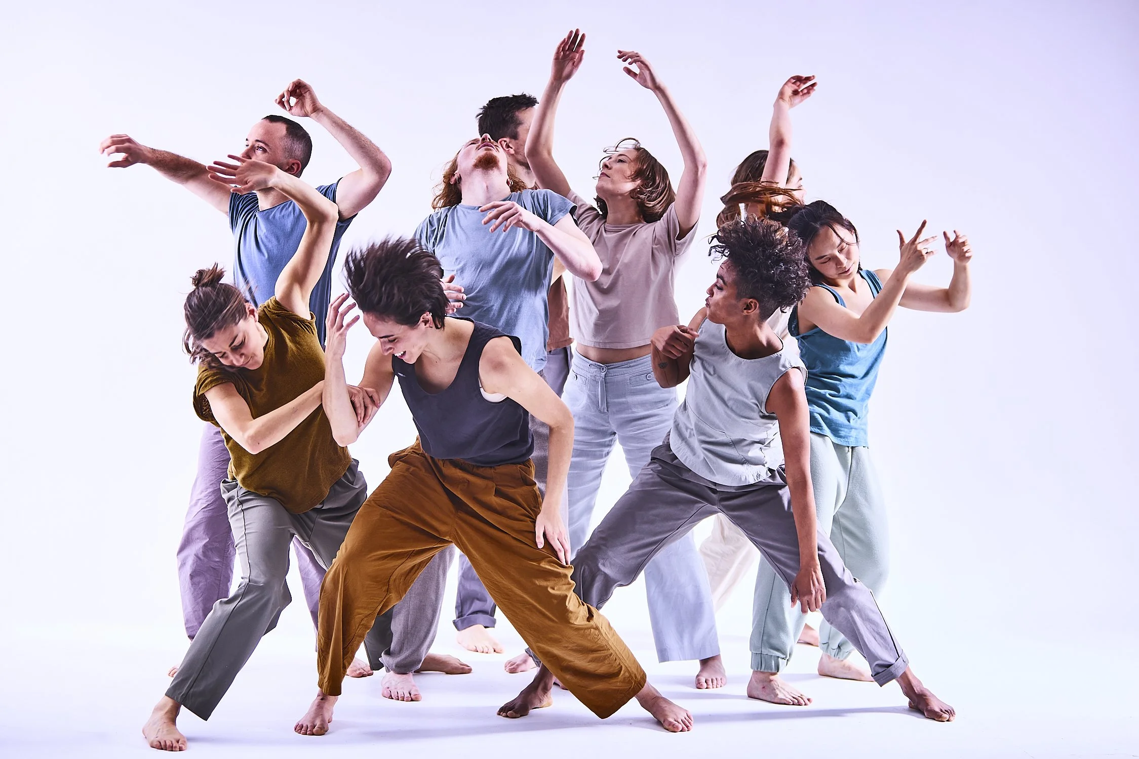 Advertising profession photo taken in studio of a group of nine diverse dancers in casual clothing practicing contemporary dance against a plain white background.