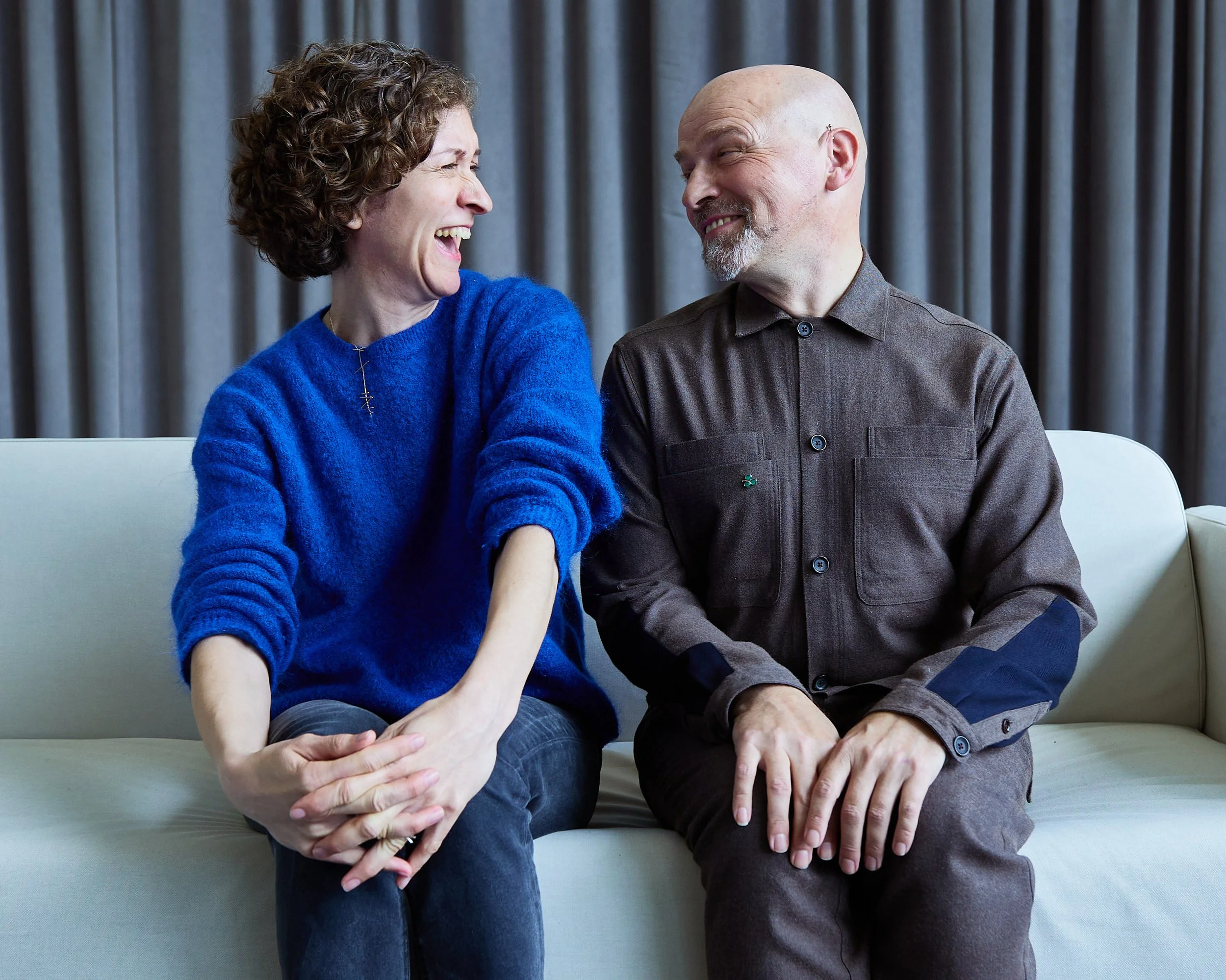 A woman and a man sitting on a couch, laughing and looking at each other.