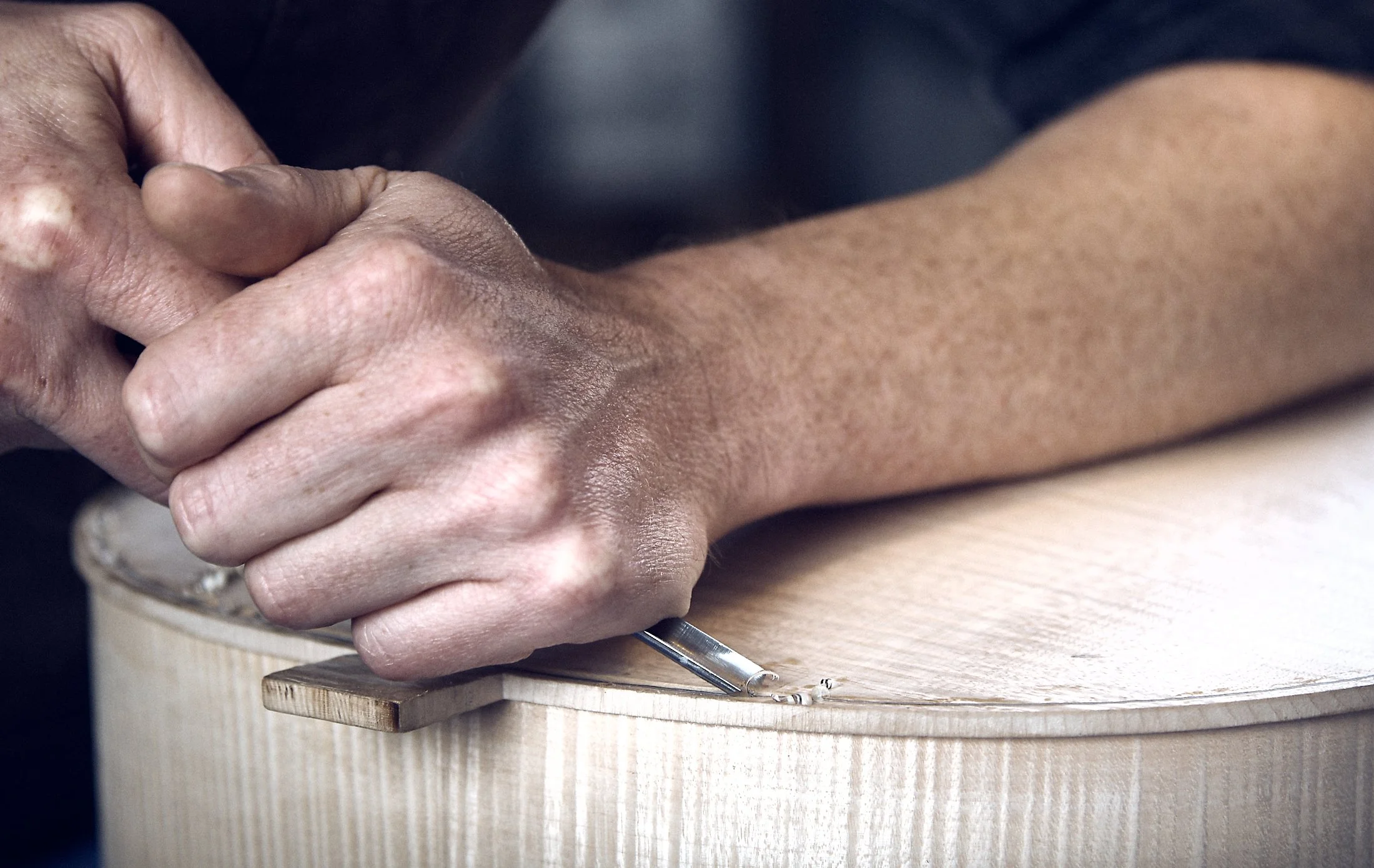 Close-up of a person's hand carving wood with a chisel, working on a wooden guitar body.