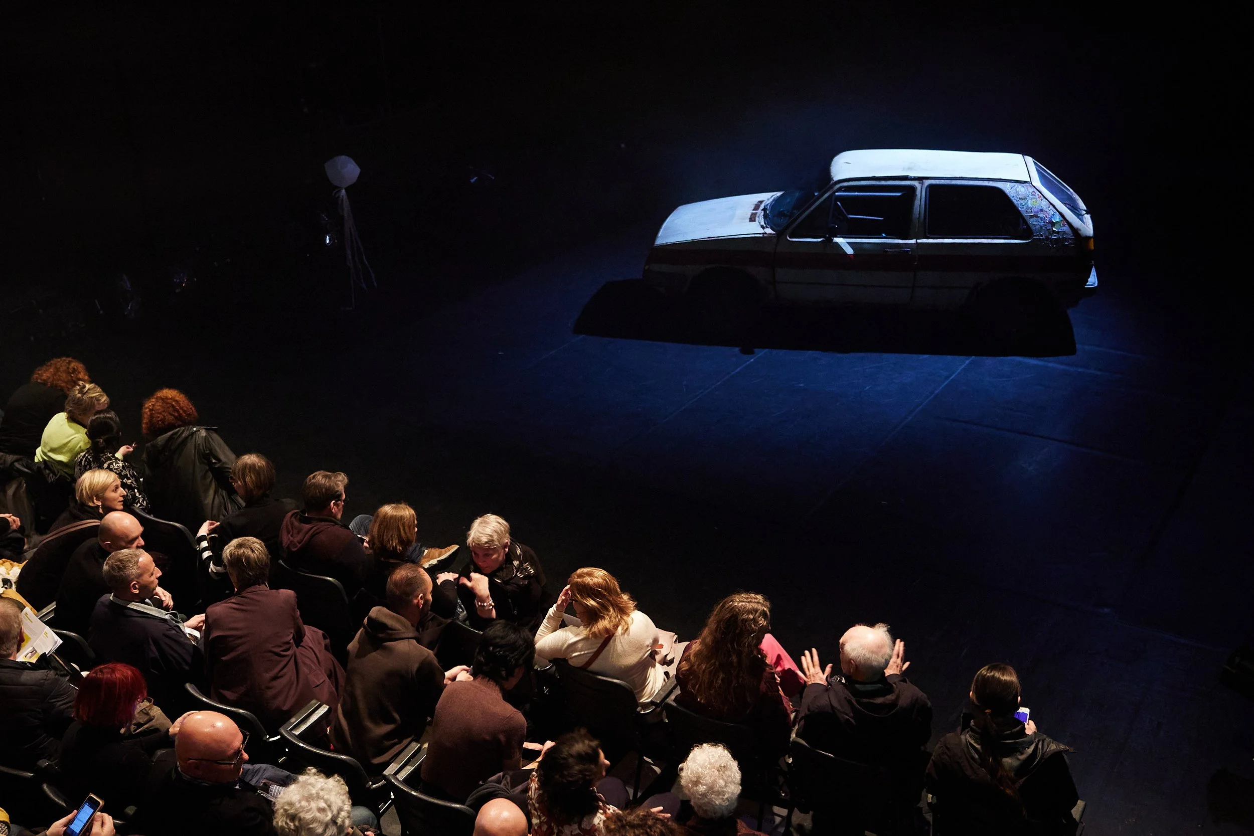 Audience watching a vintage car on display during a show.