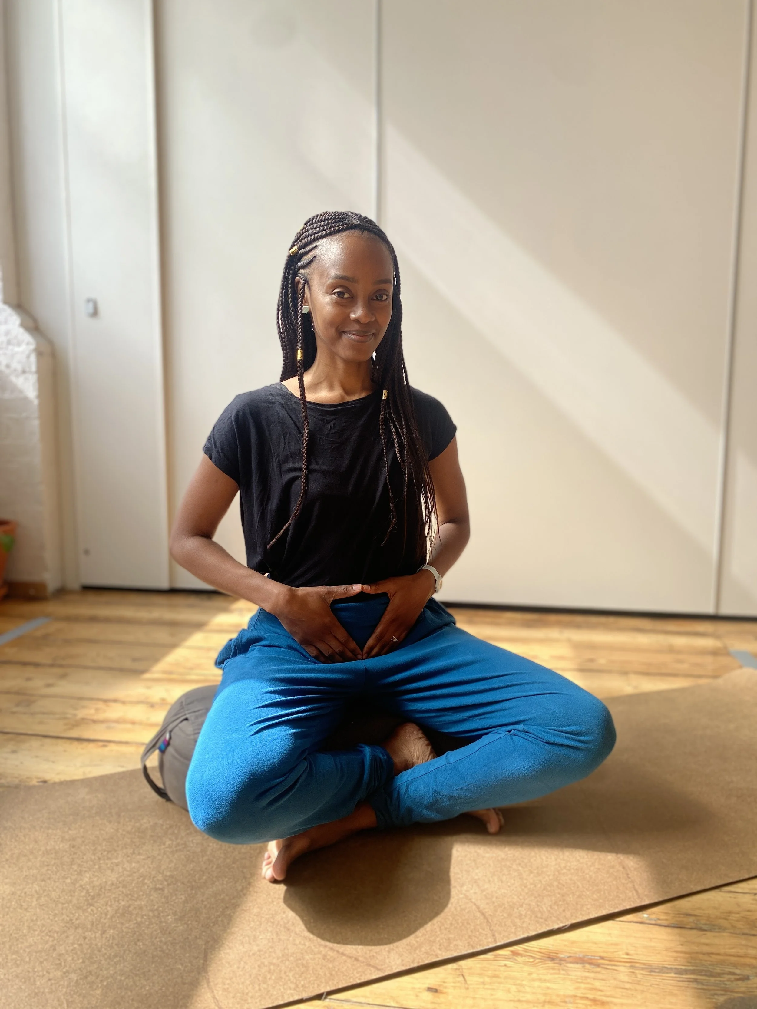 Fertility Coach sitting in yoga studio hands in yoni mudra with warm gentle smile