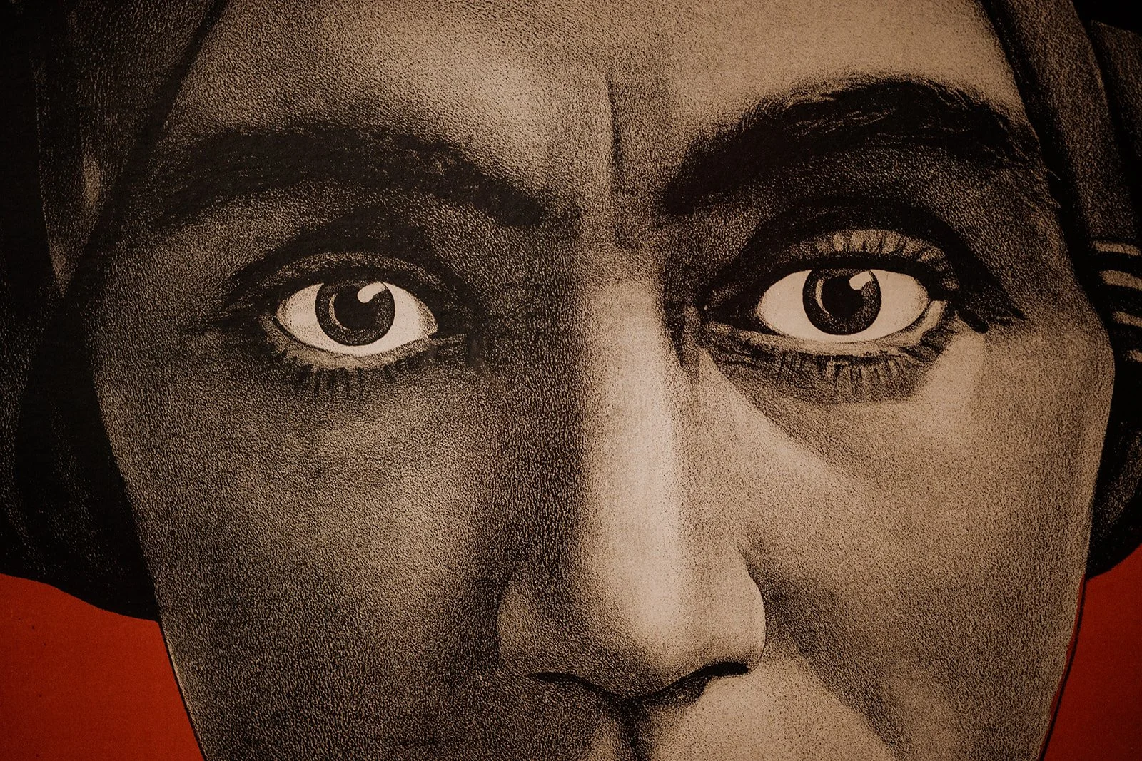 Close-up of a black-and-white vintage-style photograph of a woman’s face, showing her eyes, nose, and part of her forehead, with a red background.