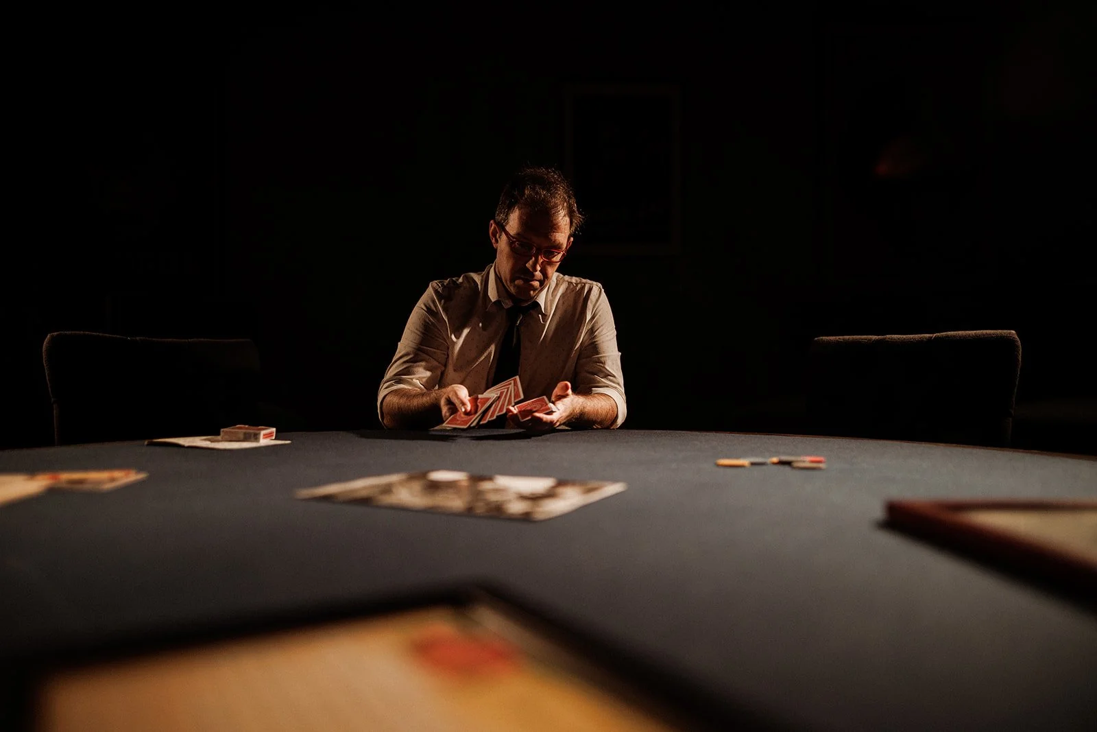 Helder Guimarães sitting at a dark table playing cards in a dimly lit room.