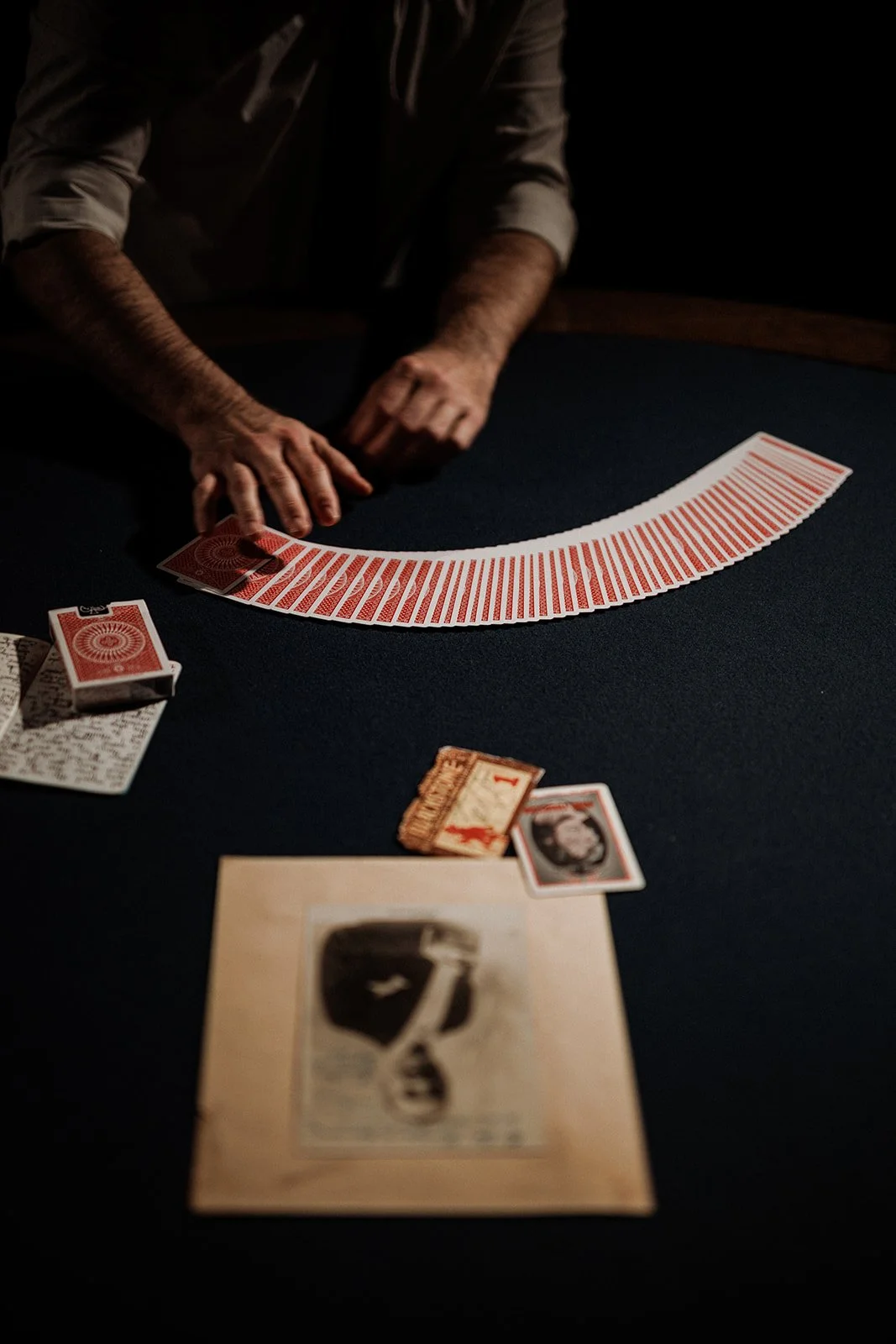 Helder Guimarães arranging a deck of playing cards on a dark table, with some cards and a vintage photograph in the foreground.
