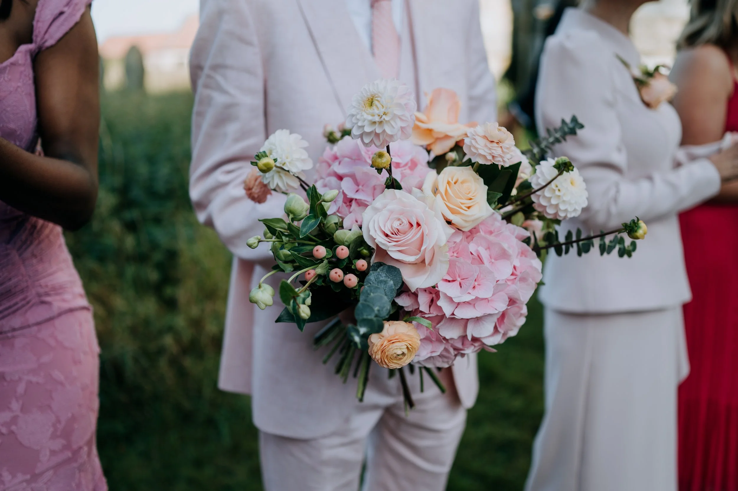 Person holding a bouquet of pink and cream-colored roses and hydrangeas at an outdoor event. East Yorkshire based wedding florals, handcrafted wedding flowers.