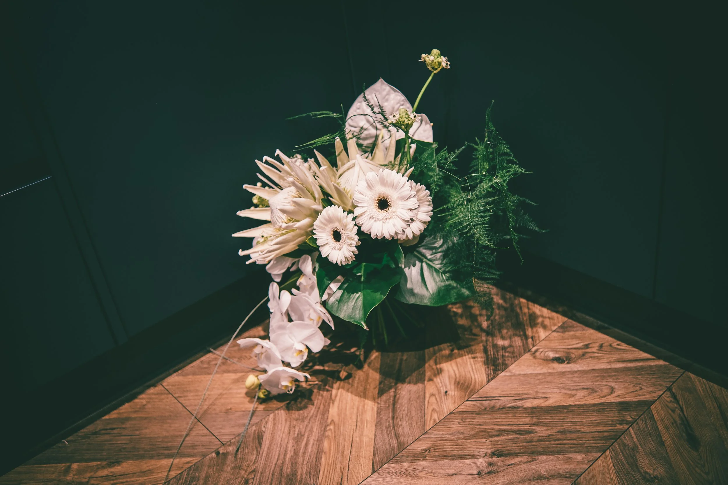 A bouquet of white flowers resting against a dark green wall and on a wooden floor. East Yorkshire based wedding florals, handcrafted wedding flowers.