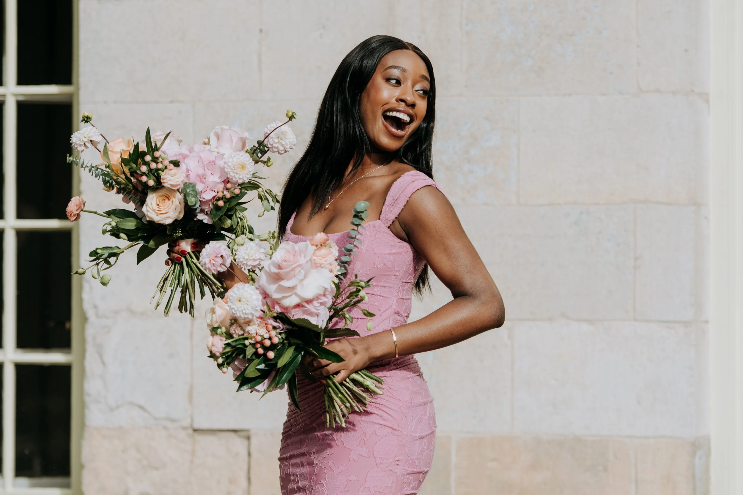 A woman in a pink dress holding a large bouquet of pink and white flowers, smiling and looking away. East Yorkshire based wedding florals, handcrafted wedding flowers.