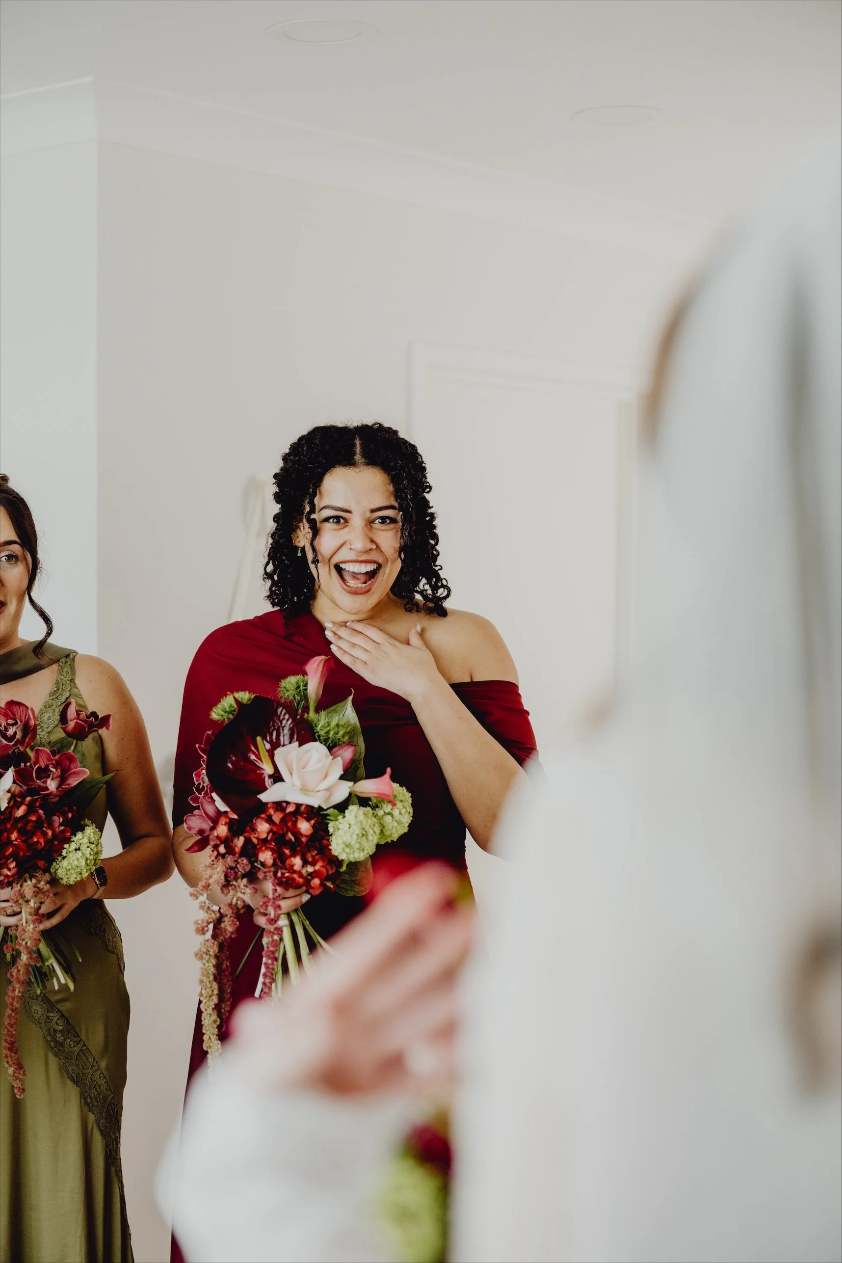 Woman in red dress with a surprised happy expression, holding a bouquet, at a celebration event.