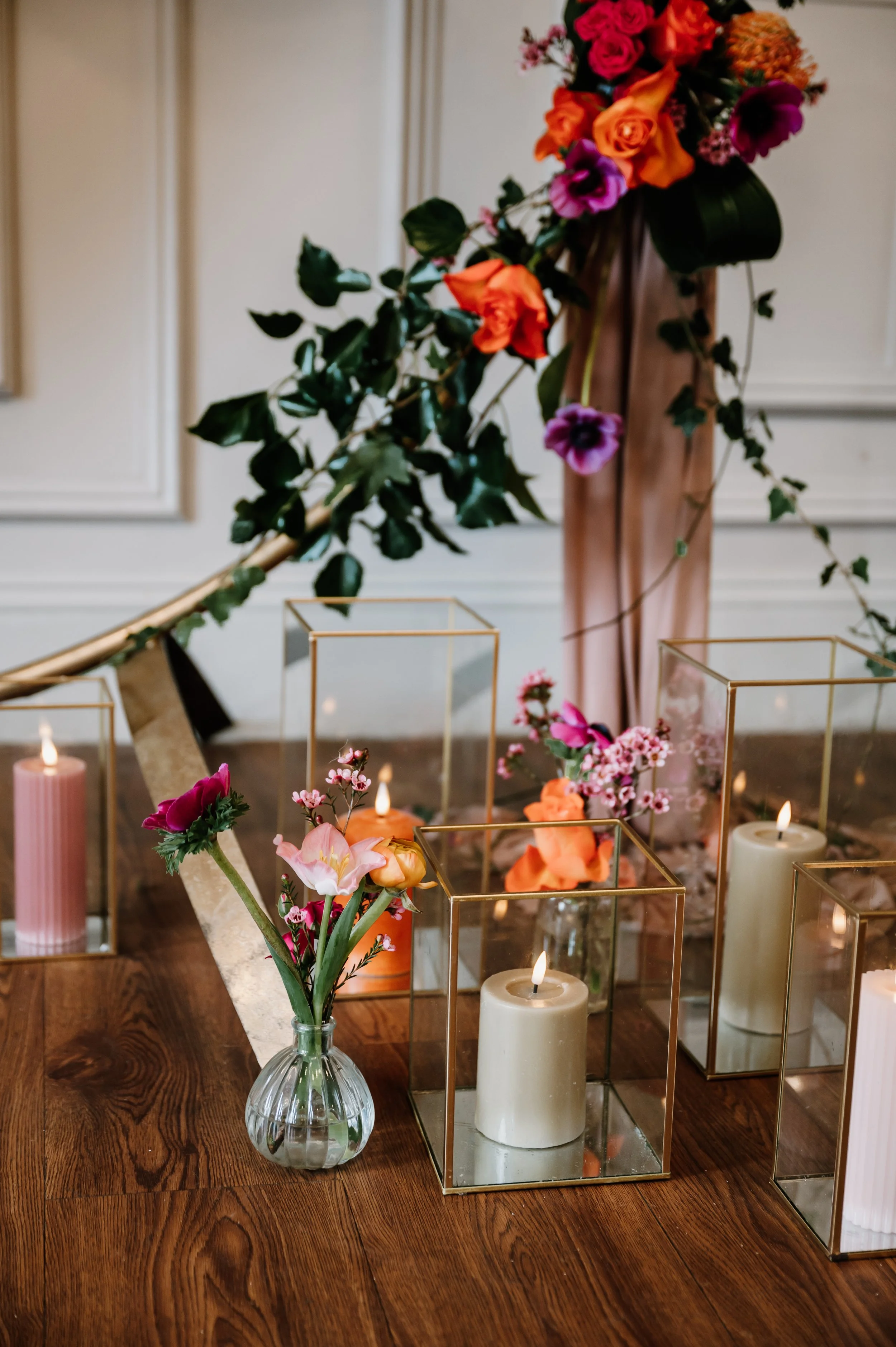 Table decorated with candles and flower arrangements, featuring a tall flower arrangement of orange, pink, and purple flowers, and smaller vases with mixed flowers, set on a wooden table with a decorative background. East Yorkshire based wedding 