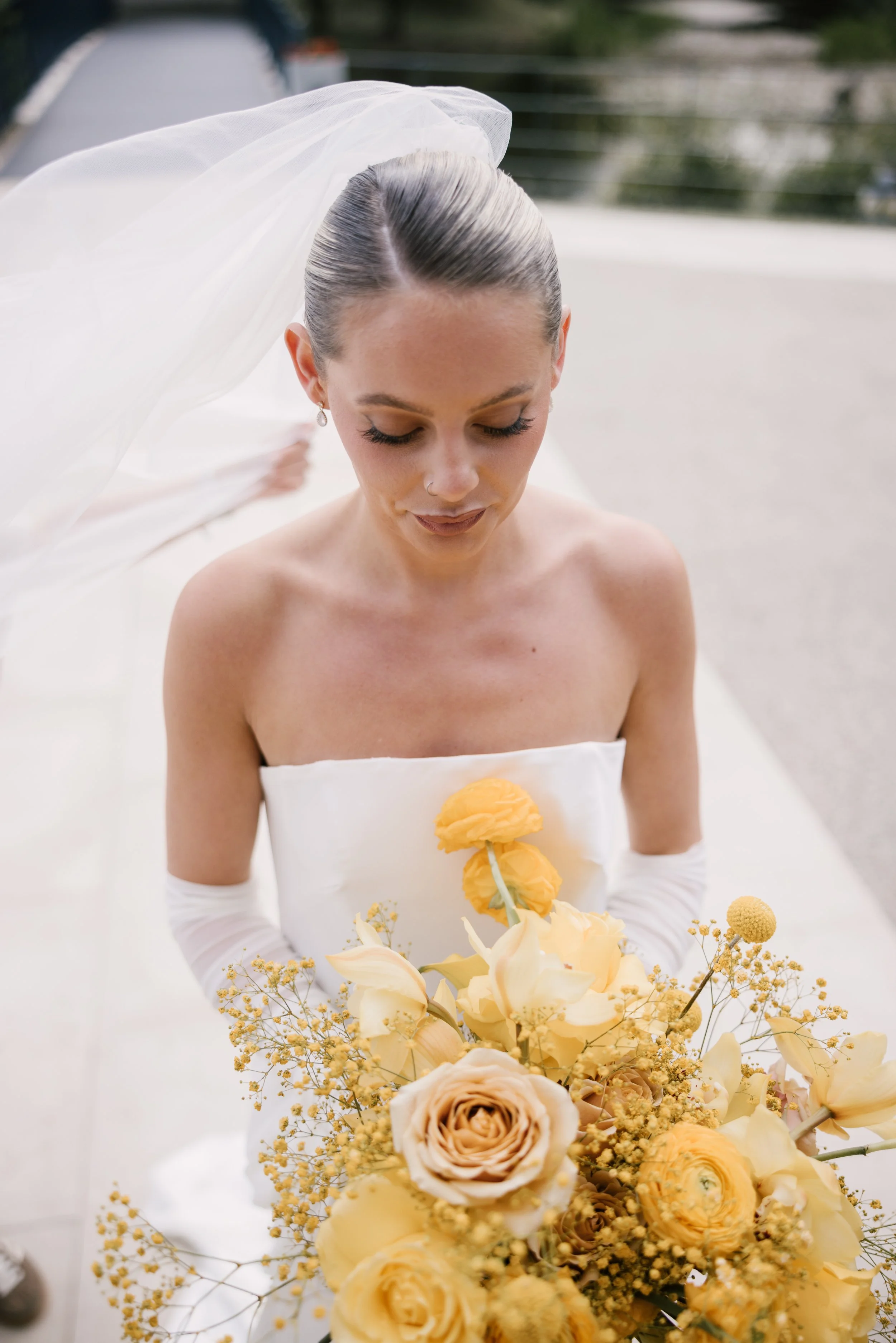 Bride with a silky white strapless wedding dress, holding a large yellow and cream bouquet, with her eyes closed and veil flowing behind her. East Yorkshire based wedding florals, handcrafted wedding flowers.