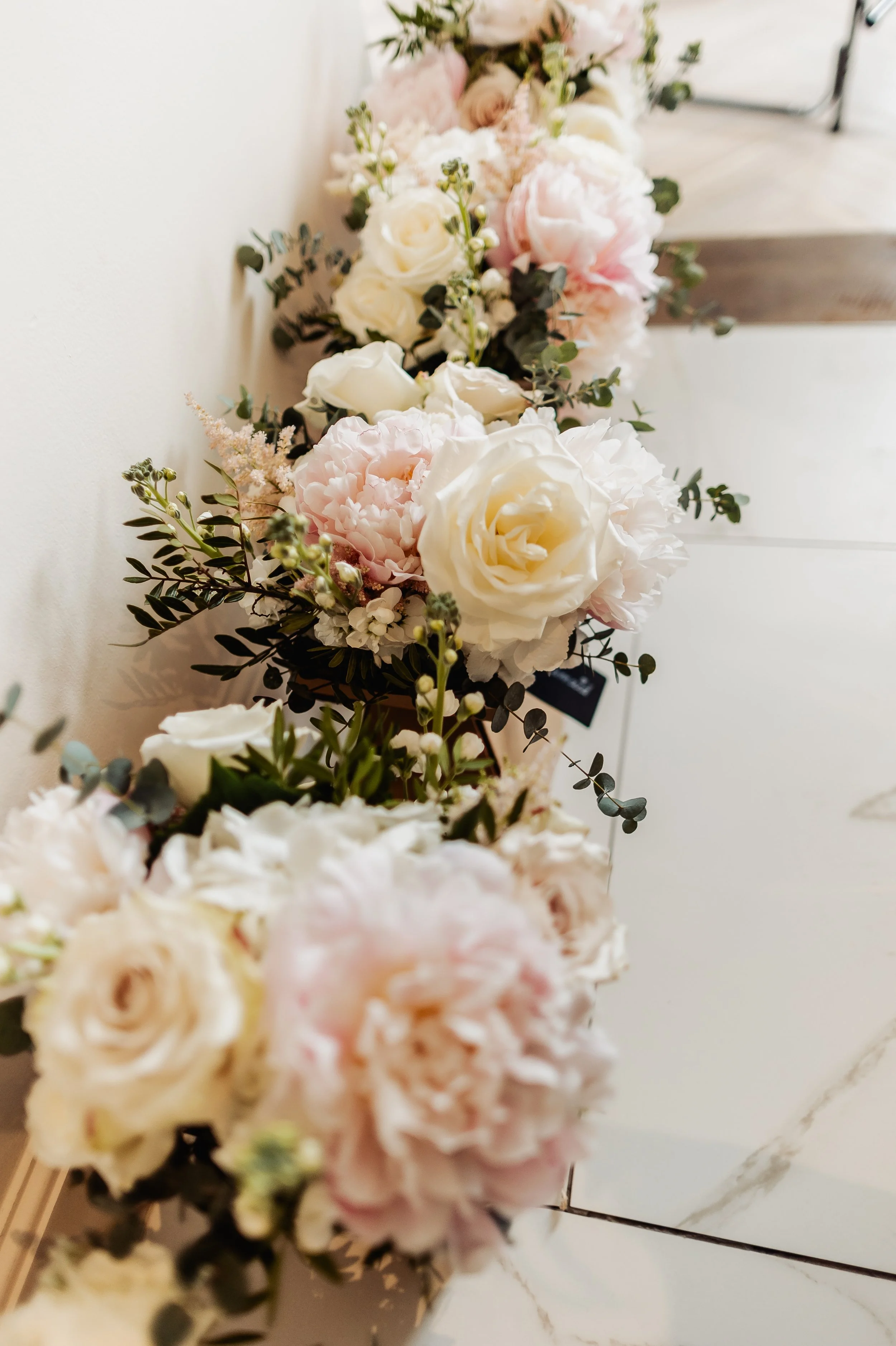 A close-up of a floral garland featuring white and pink roses, peonies, and greenery, lying on a white surface. East Yorkshire based wedding florals, handcrafted wedding flowers.