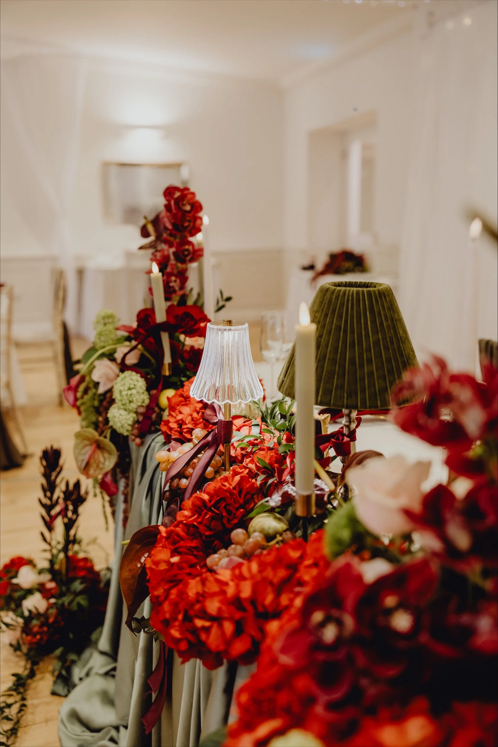 Decorative floral centerpiece on a wedding or event table with lamps and candles in a well-lit room.