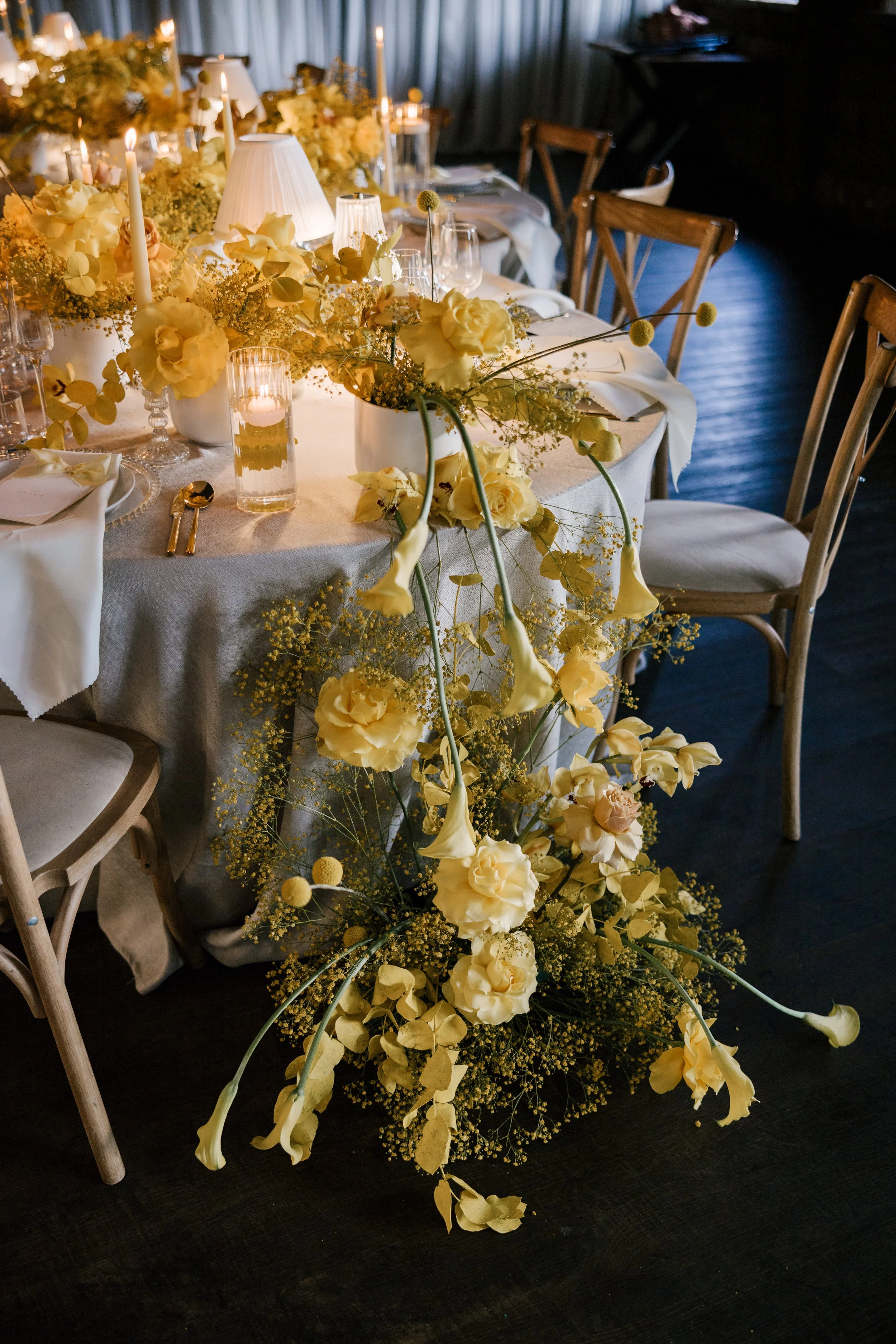 Elegant wedding table decorated with a cascading centerpiece of yellow flowers and candles, set with white napkins, glassware, and gold utensils. East Yorkshire based wedding florals, handcrafted wedding flowers.
