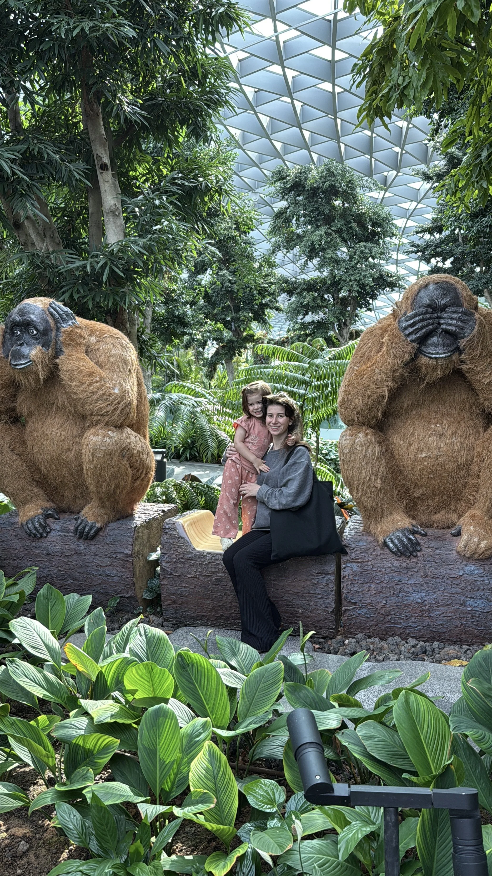 chloe and athena sitting between orangutan topiaries inside jewel changi airport indoor rainforest in singapore 