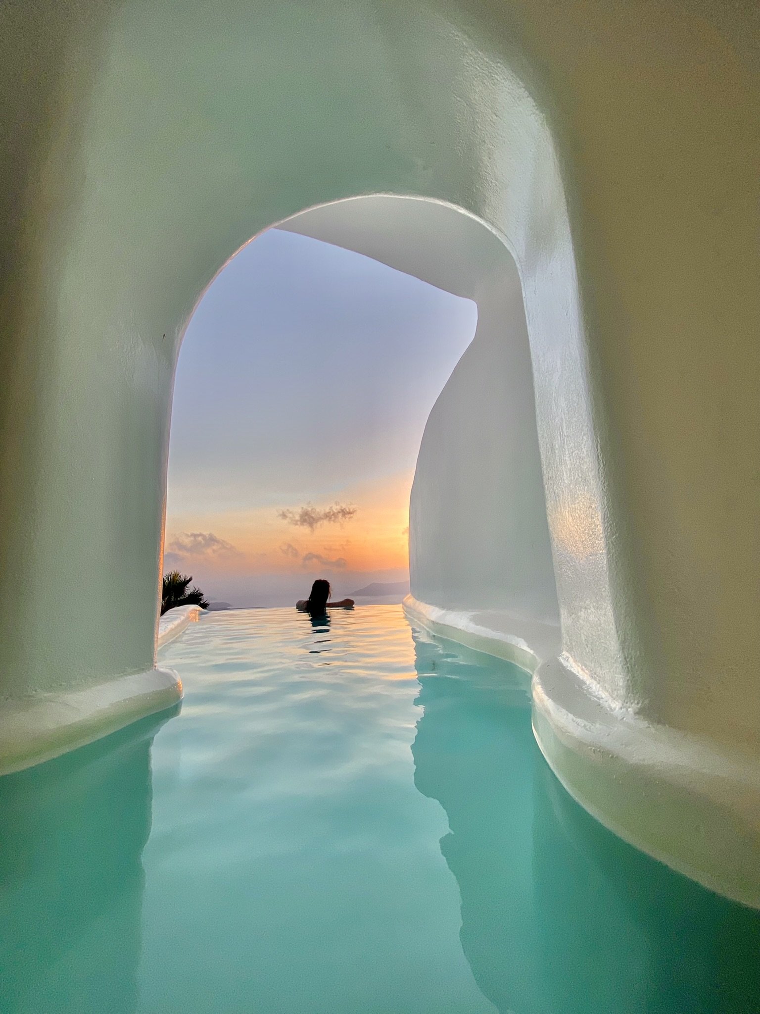 Luxury infinity pool overlooking the ocean at sunset with a person relaxing in the water.