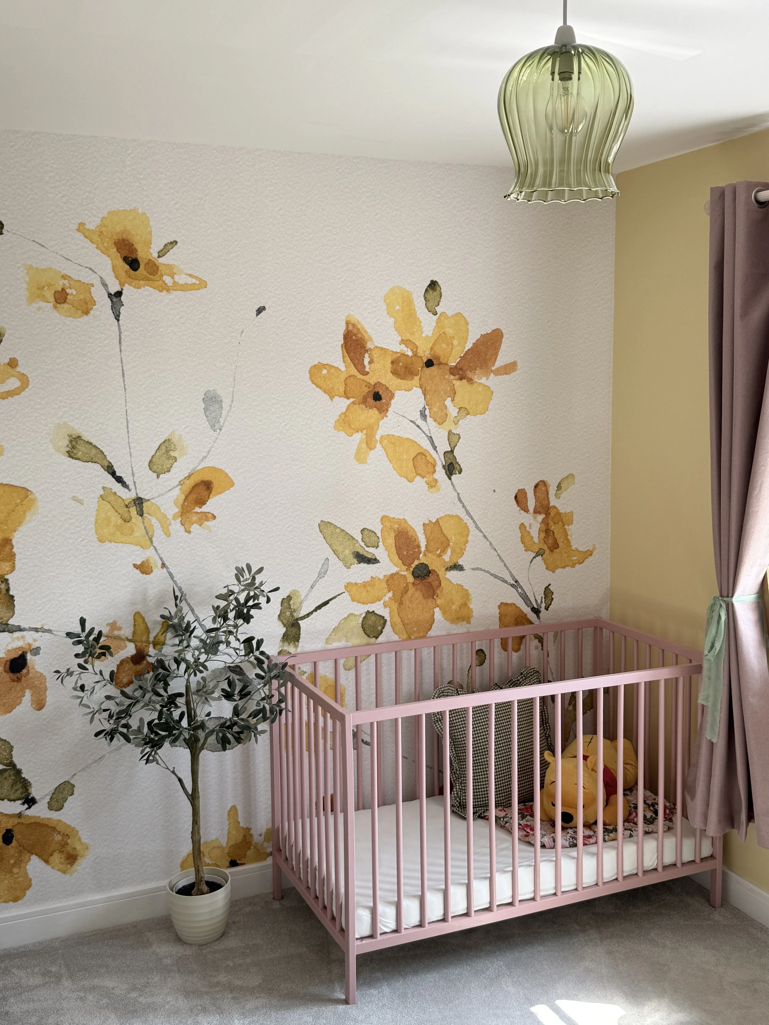 Modern children's nursery with floral wall mural, pink cot and stylish family-friendly décor.