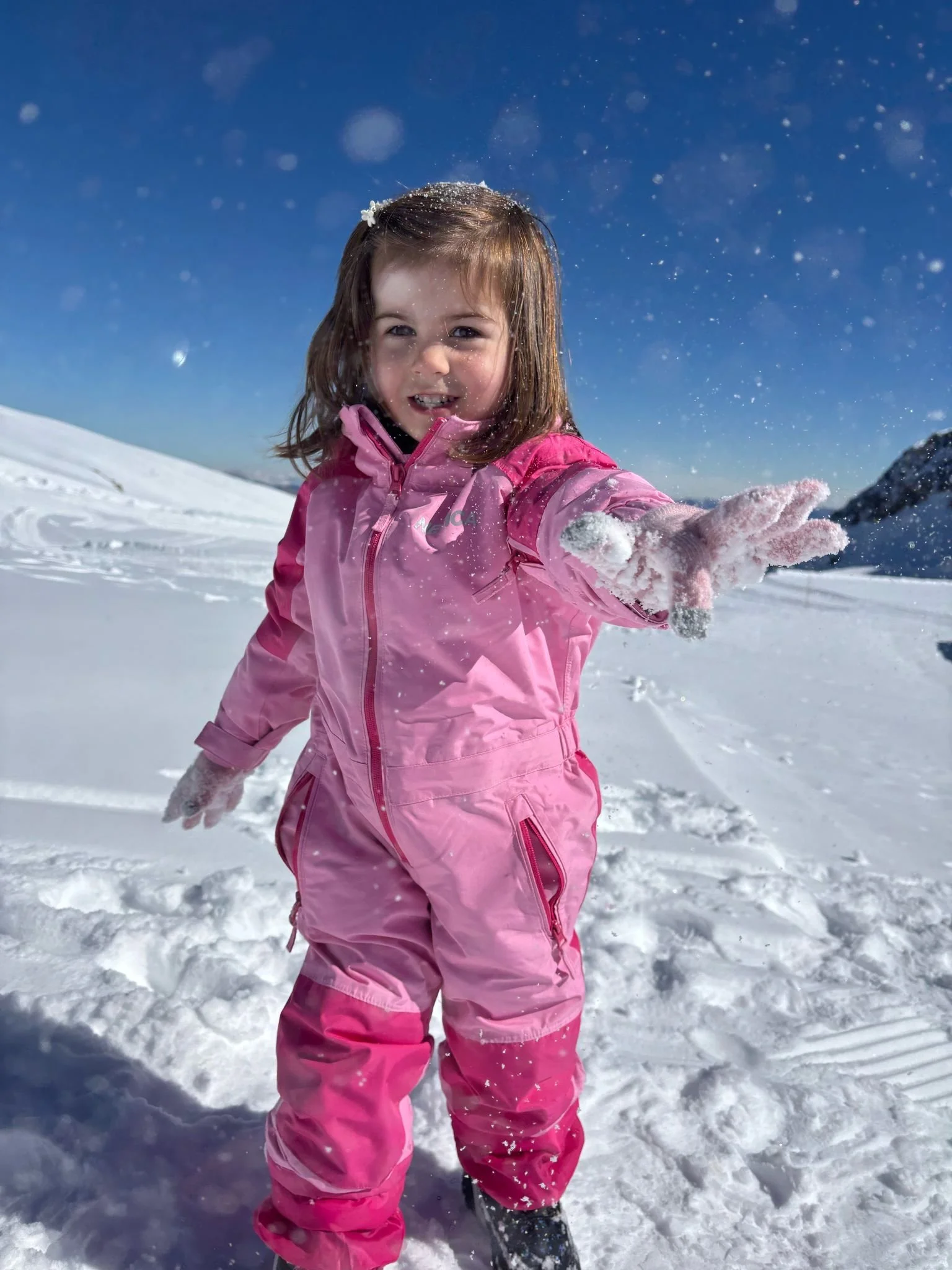 Young child wearing pink ski clothing playing happily in the snow during a family winter holiday.