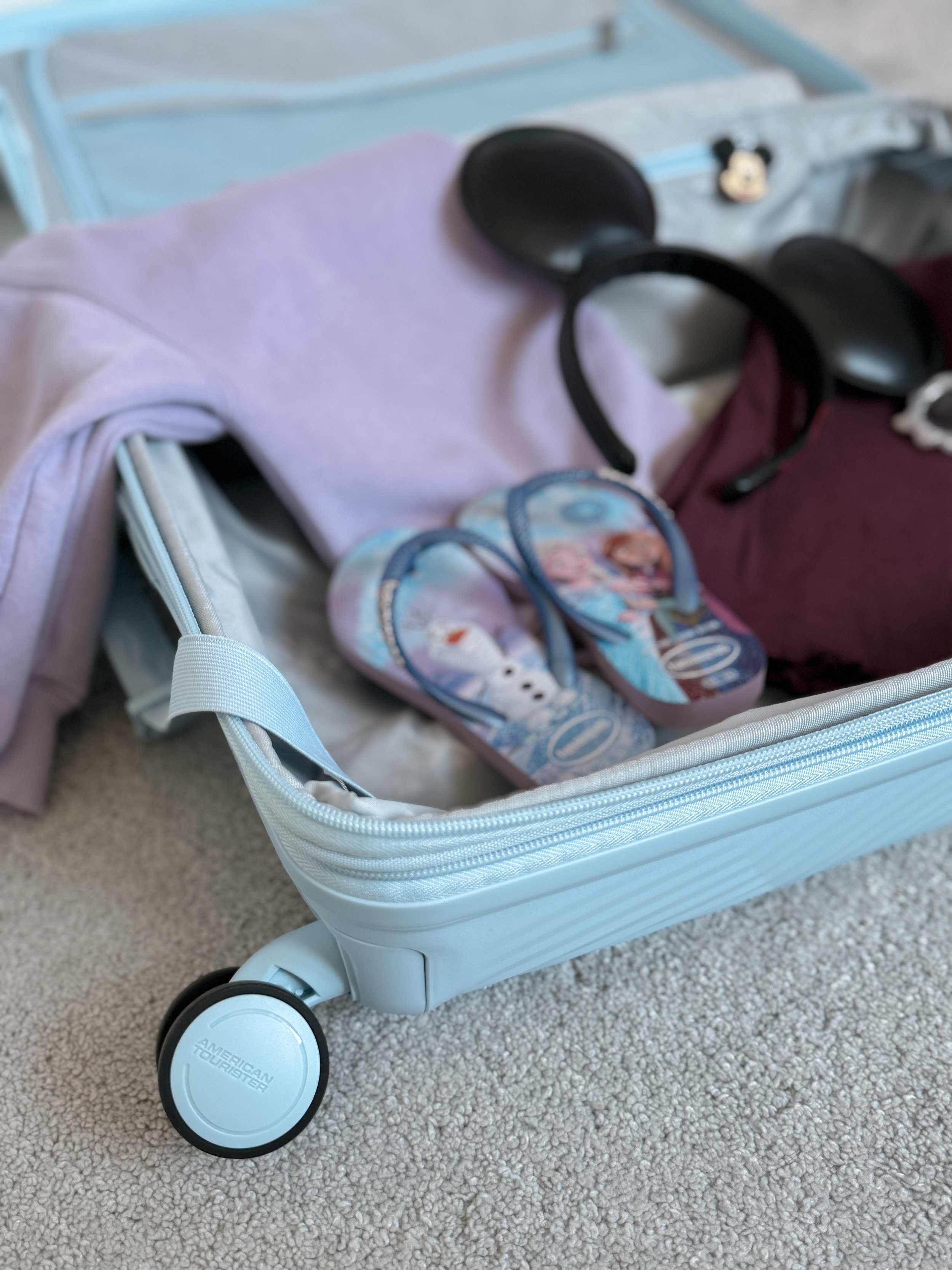 Family travel suitcase packed with children's essentials including Minnie Mouse ears and travel accessories.
