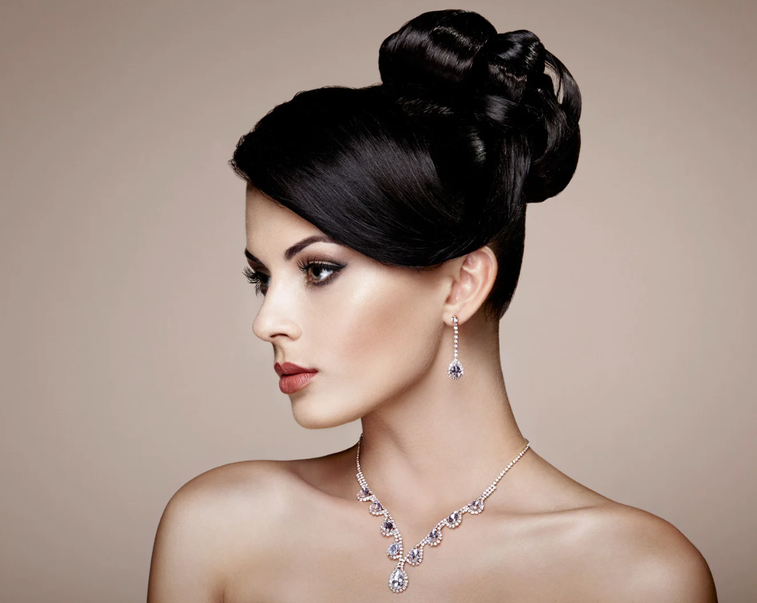 Una donna con capelli raccolti in un'acconciatura elegante indossa orecchini, collana e braccialetti di gioielli scintillanti.