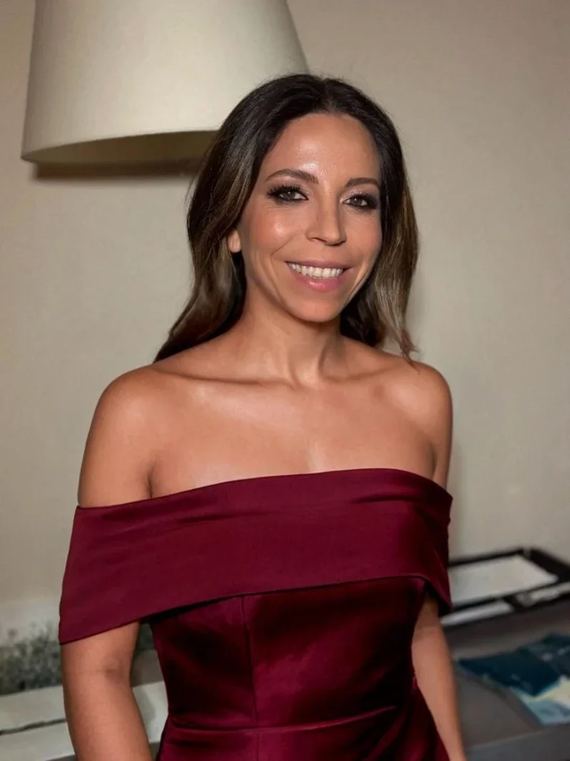 Donna sorridente con vestito rosso bordo, sfondo di parete e lampada