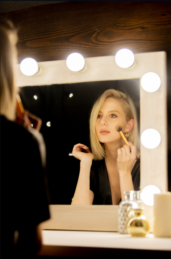 Una donna con capelli biondi corti si trucca davanti a uno specchio con luciLED, in un ambiente luminato e elegante.
