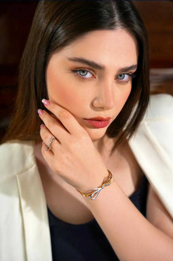 Ragazza con occhi azzurri che indossa una collana e un anello, con una giacca chiara e sfondo in legno