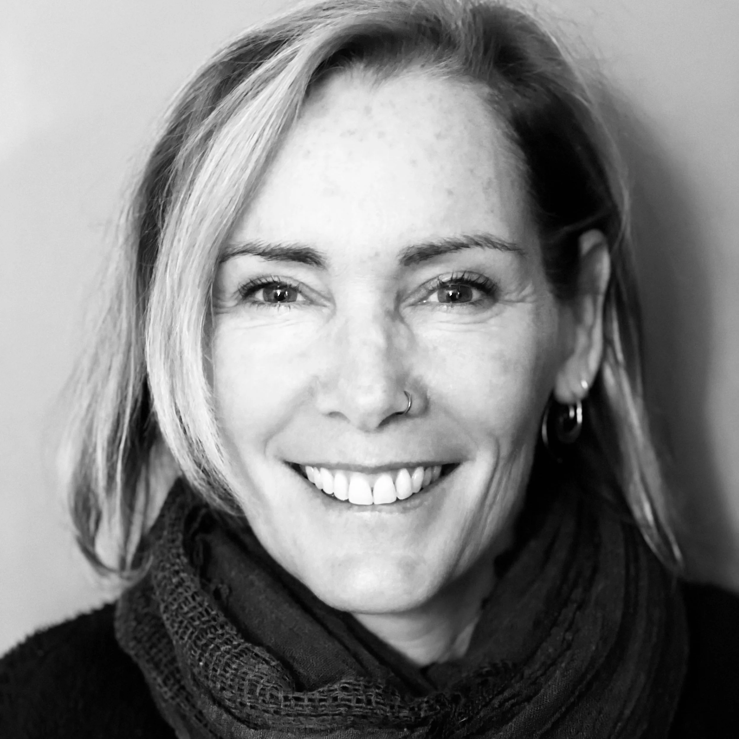 Black and white photo of a woman smiling showing her teeth, with hair parted to the side, wearing earrings and a shawl or scarf.