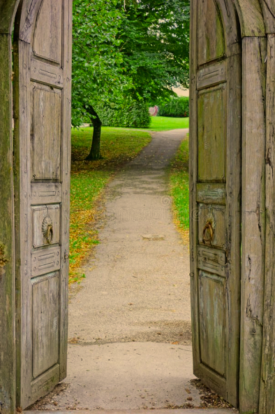 Wooden open door looking out onto a gravel path through a green park with trees and grass.