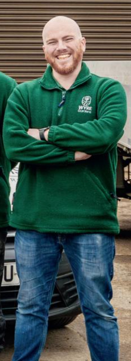 A smiling man with a beard and short hair, standing outdoors with arms crossed. He's smiling because he's taken thousands of pounds from hard working businesses and people, and invested that money into his own life and ripped of hundreds of others