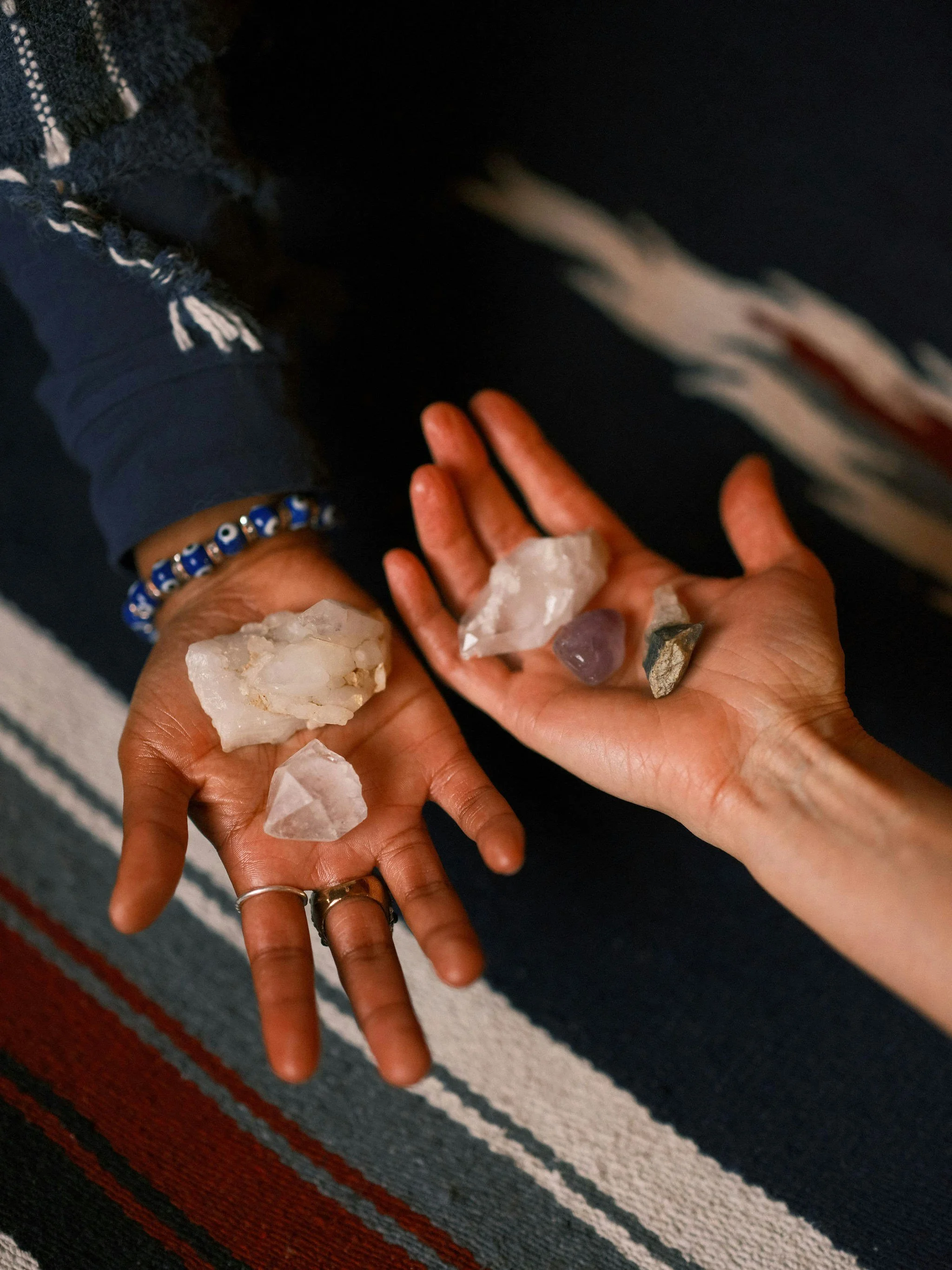 A person's hand holding a collection of various rocks and crystals over a striped rug.