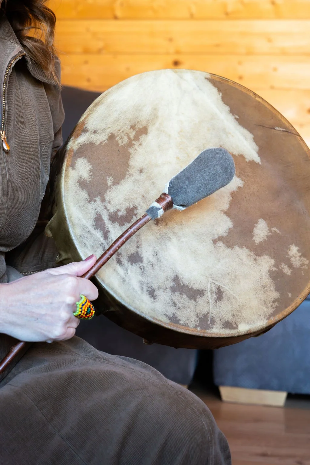 Person playing a large drum with a mallet, in a room with wooden walls.