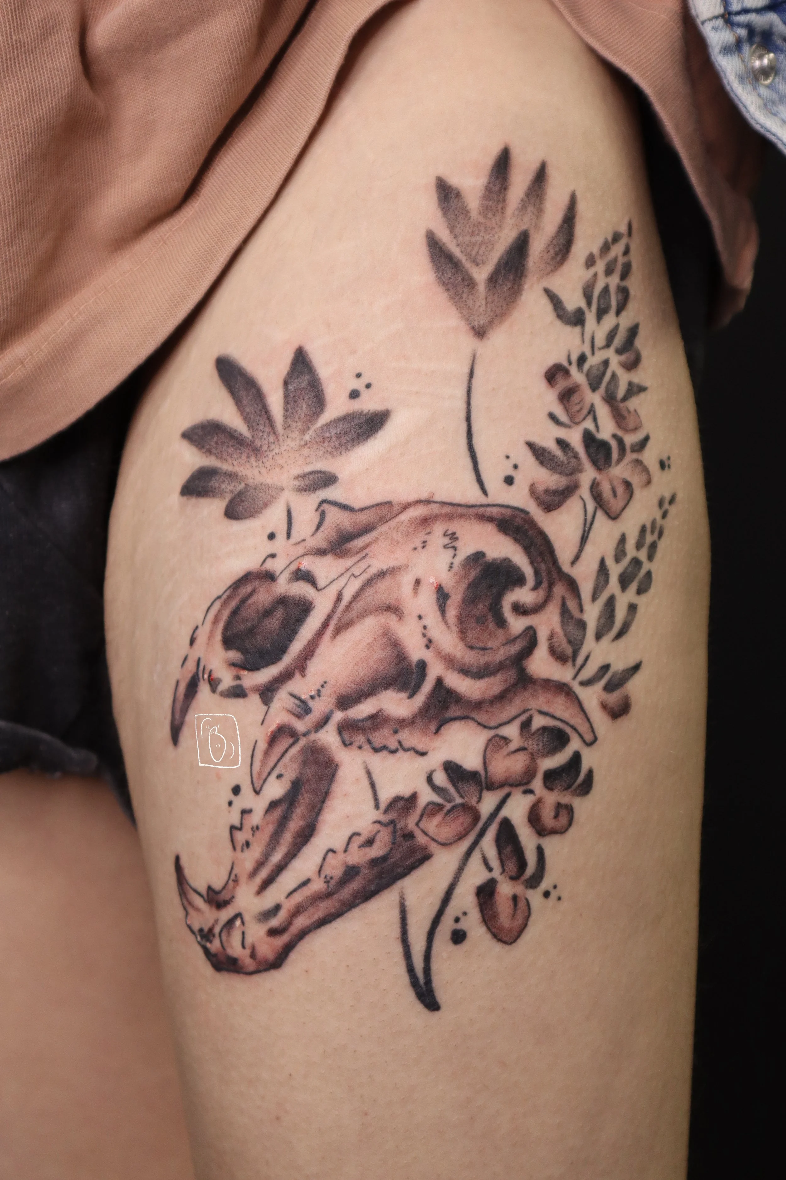 a full bear skull with its jaws open on a thigh, surrounded by lupine flowers 