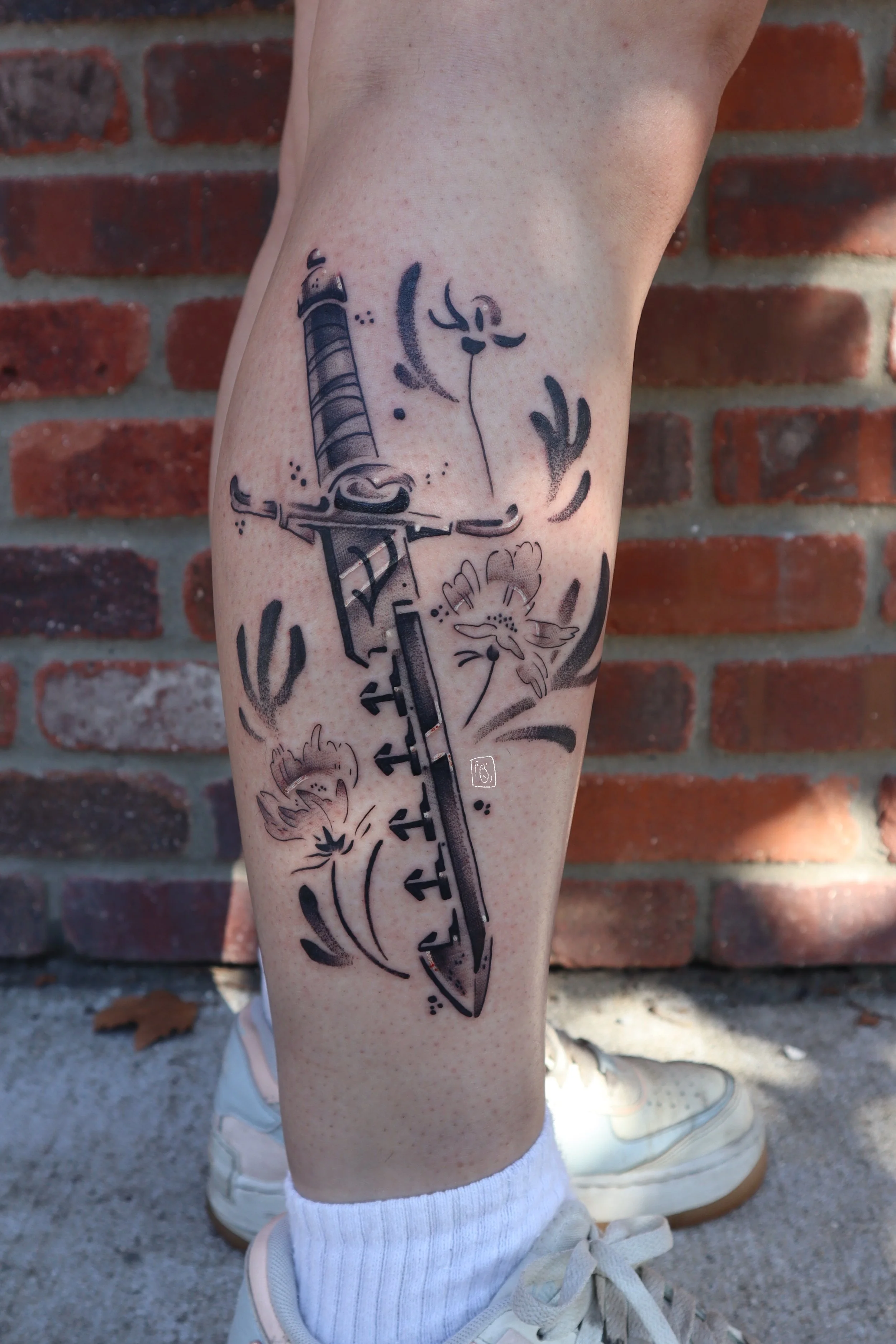 tattoo of a sword breaker dagger, surrounded by coreopsis flowers. it is on the side of a calf and is done in a soft clack and grey