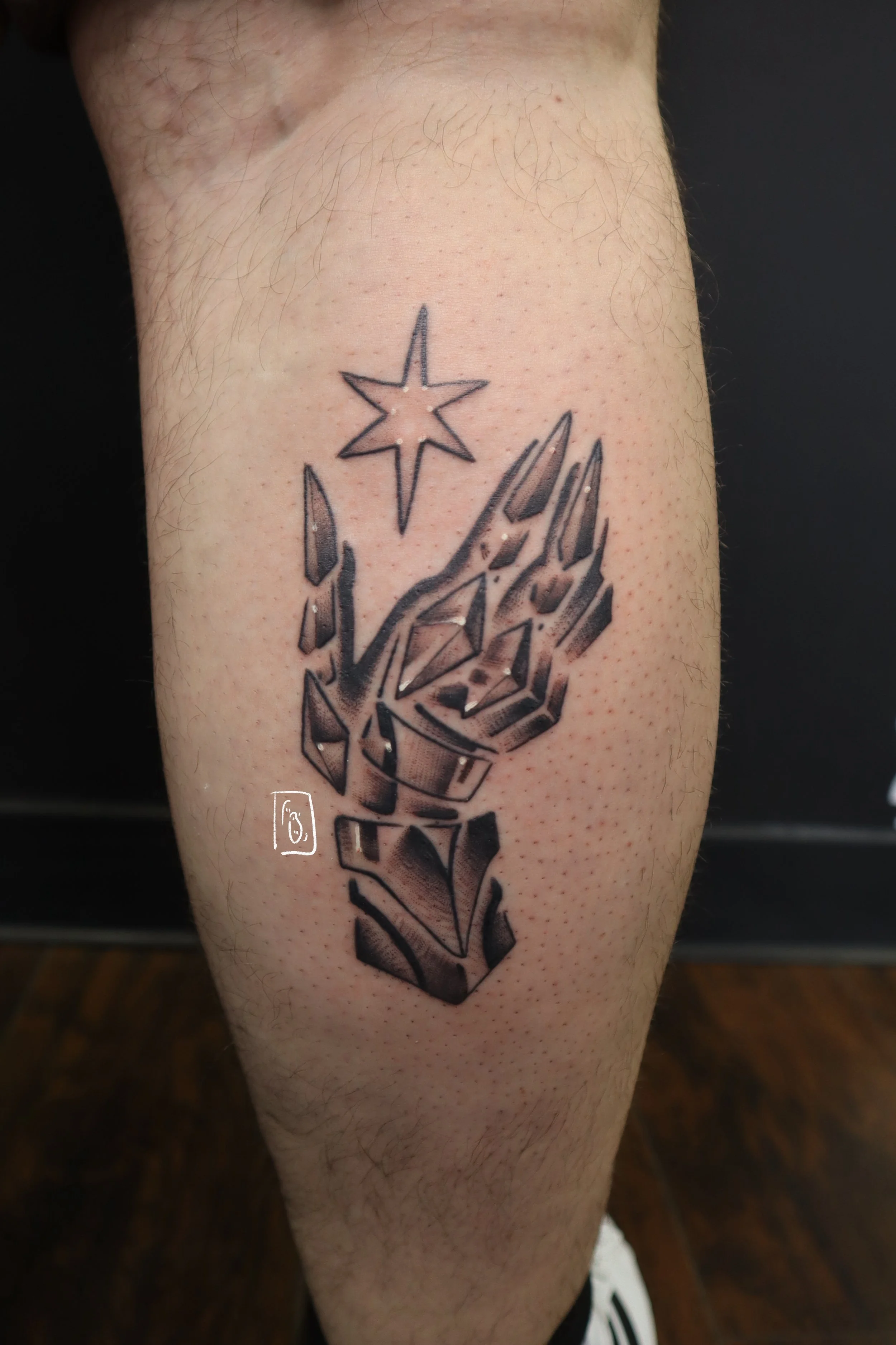 tattoo of a gauntlet reaching upward, caressing a small star. it is on the back of a calf, done in a soft black and grey illustrative style