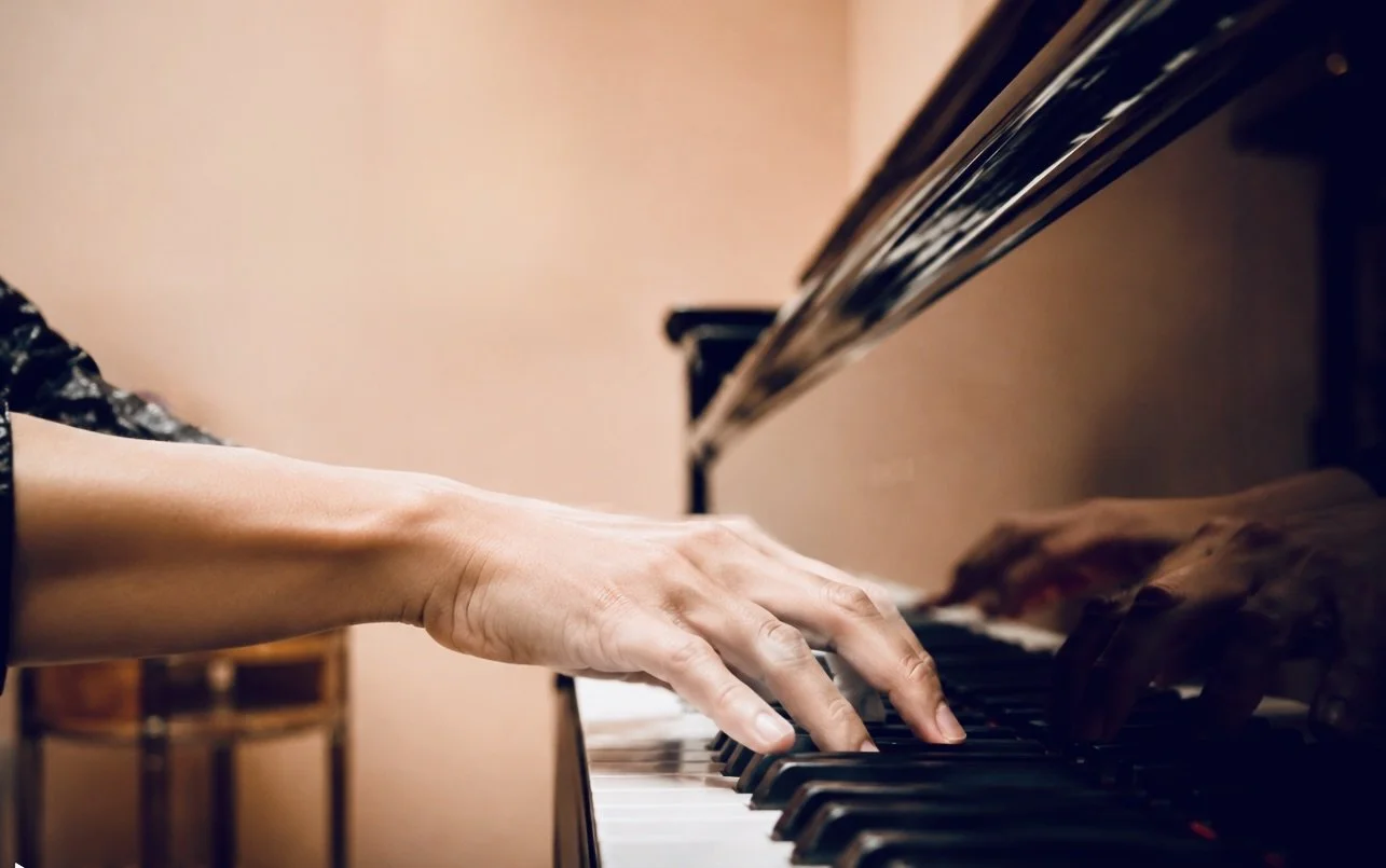 Nahaufnahme einer Person, die Klavier spielt, mit Fokus auf die Hände auf den Tasten, im Hintergrund ist die Pianofläche sichtbar.