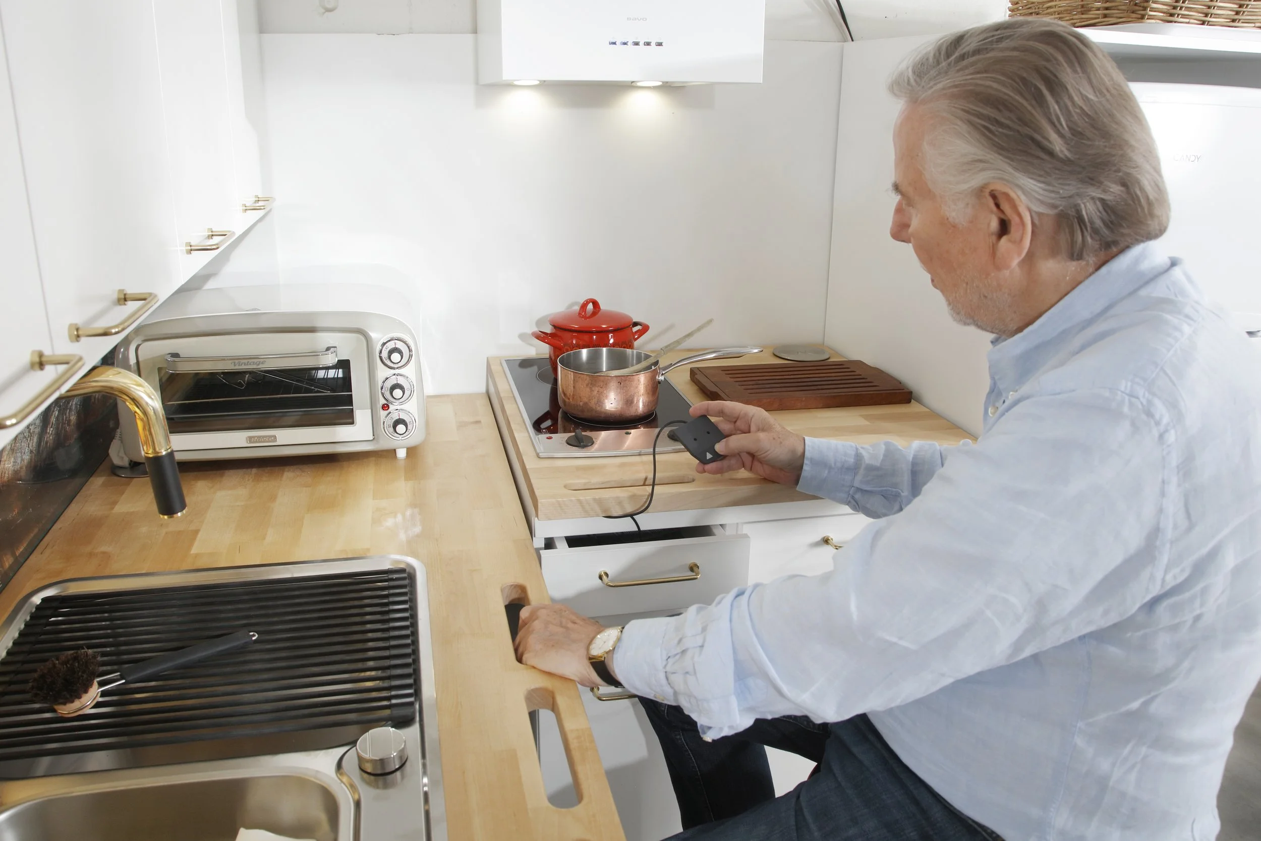 Mies keittää vettä kattilassa liesi päällä ja säätää napinpainalluksella keittiötä itselleen sopivalle korkeudelle.