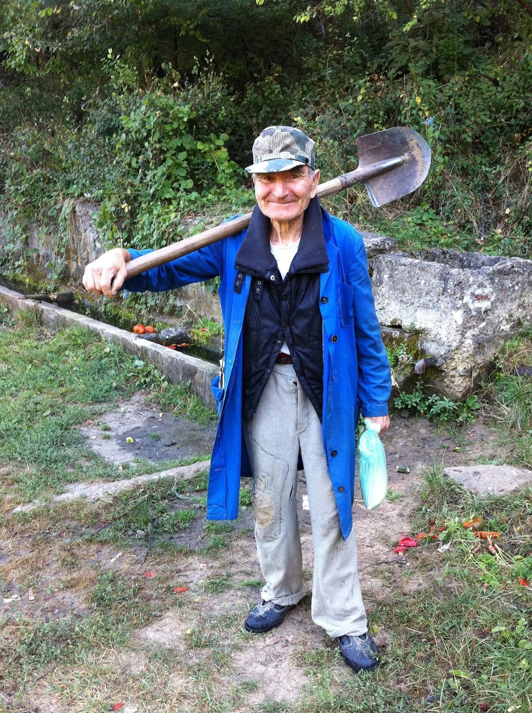 Iäkäs mies lapio olalla valmiina töihin