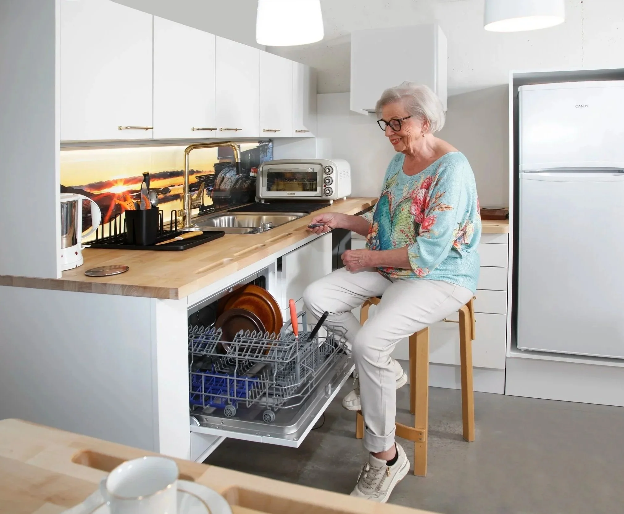 Nainen täyttää astianpesukonetta turvallisesti ottaen tukea keittiötason käsituesta.