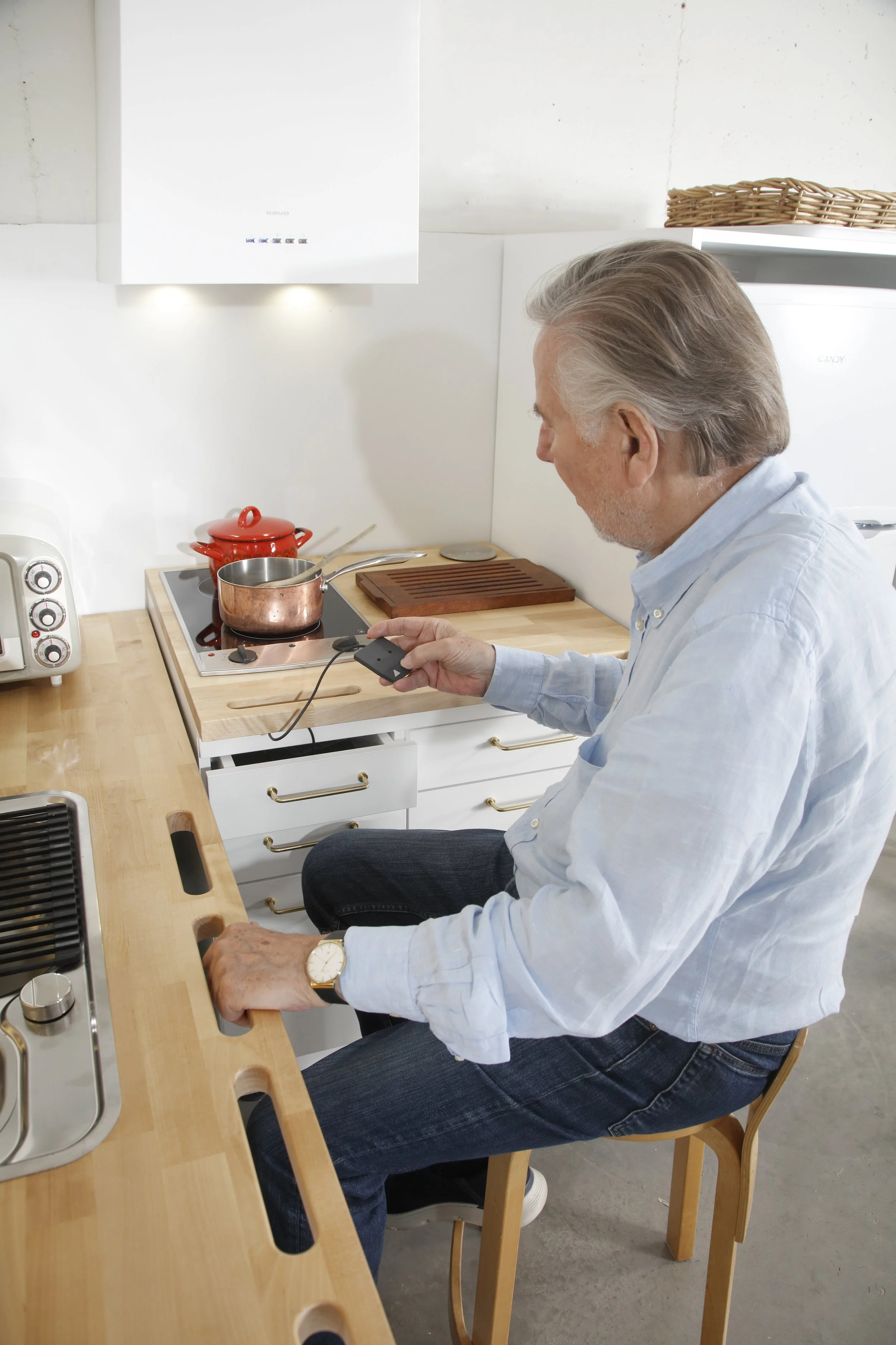 Ihminen istuu keittiönssä, katsoo laitteen kaukosäädintä.